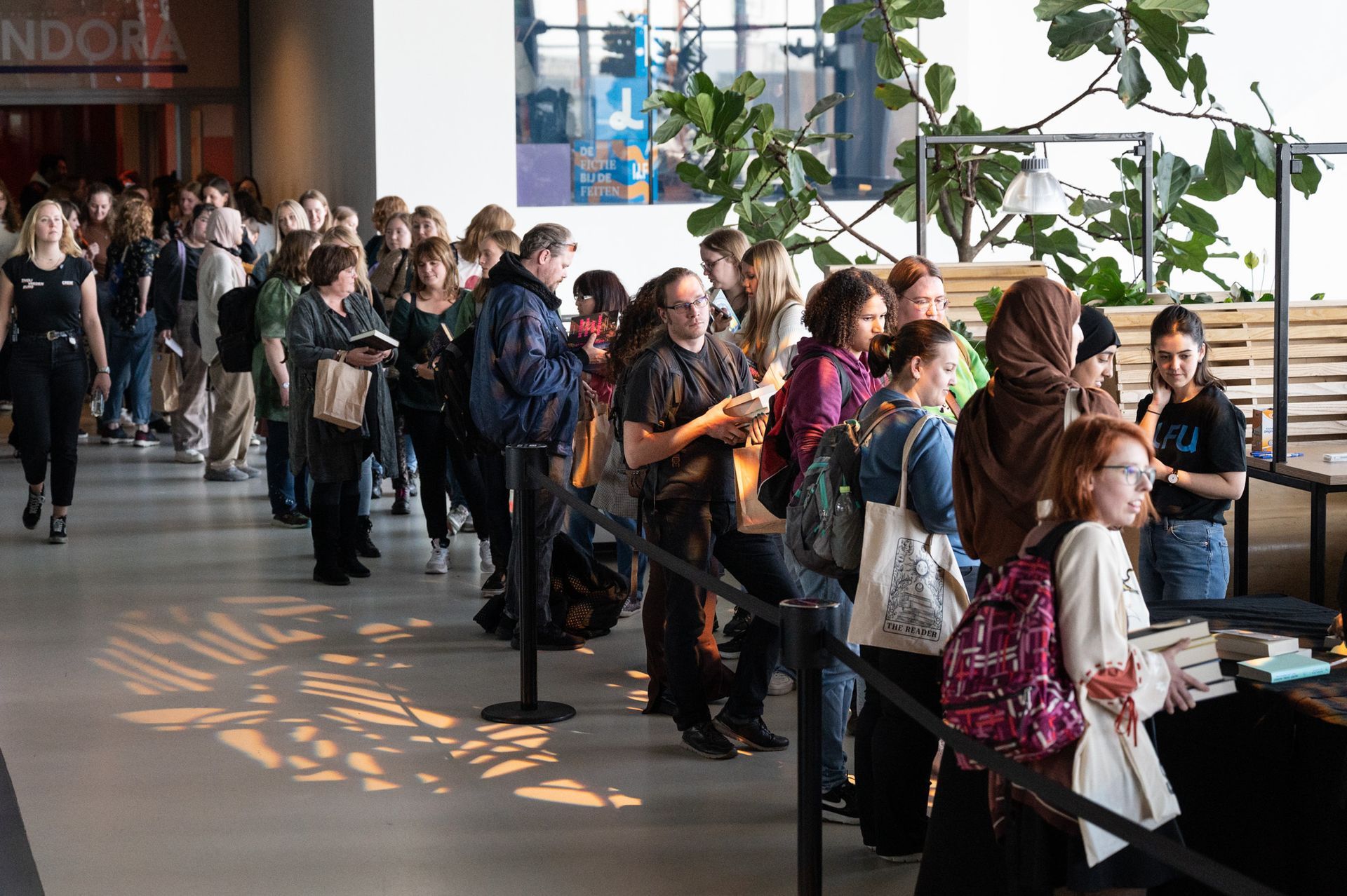 Mensen stonden met koffers in de rij bij een incheckbalie op de luchthaven, naast grote ramen.