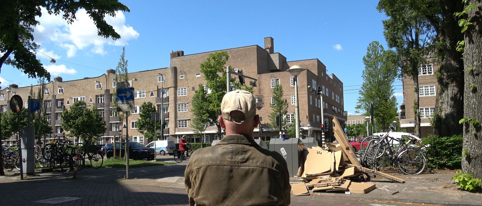 Een persoon in een camouflagejas kijkt naar beschadigde appartementencomplexen en puin onder een blauwe hemel.