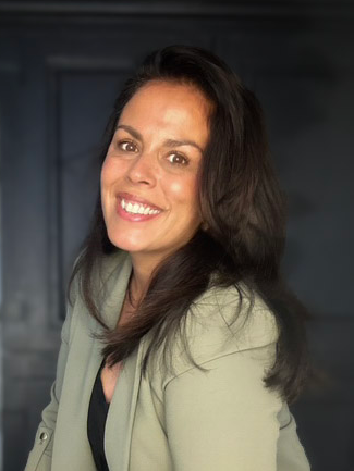 Lachende vrouw met donker haar, gekleed in een lichtgroene blazer, tegen een donkere achtergrond.