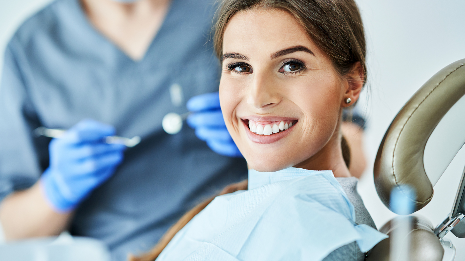 A woman is smiling while sitting in a dental chair.