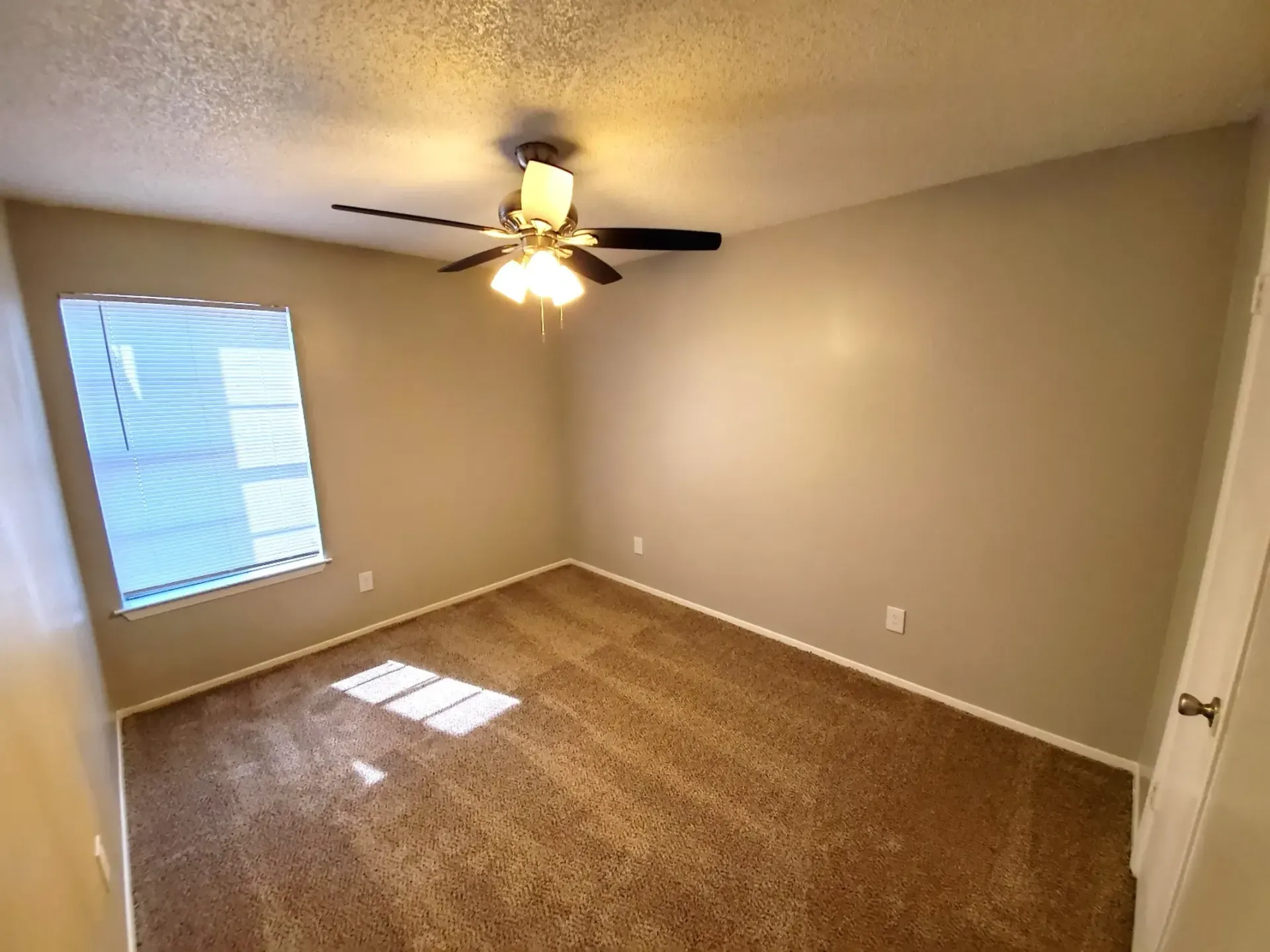 An empty bedroom with a ceiling fan and a window.