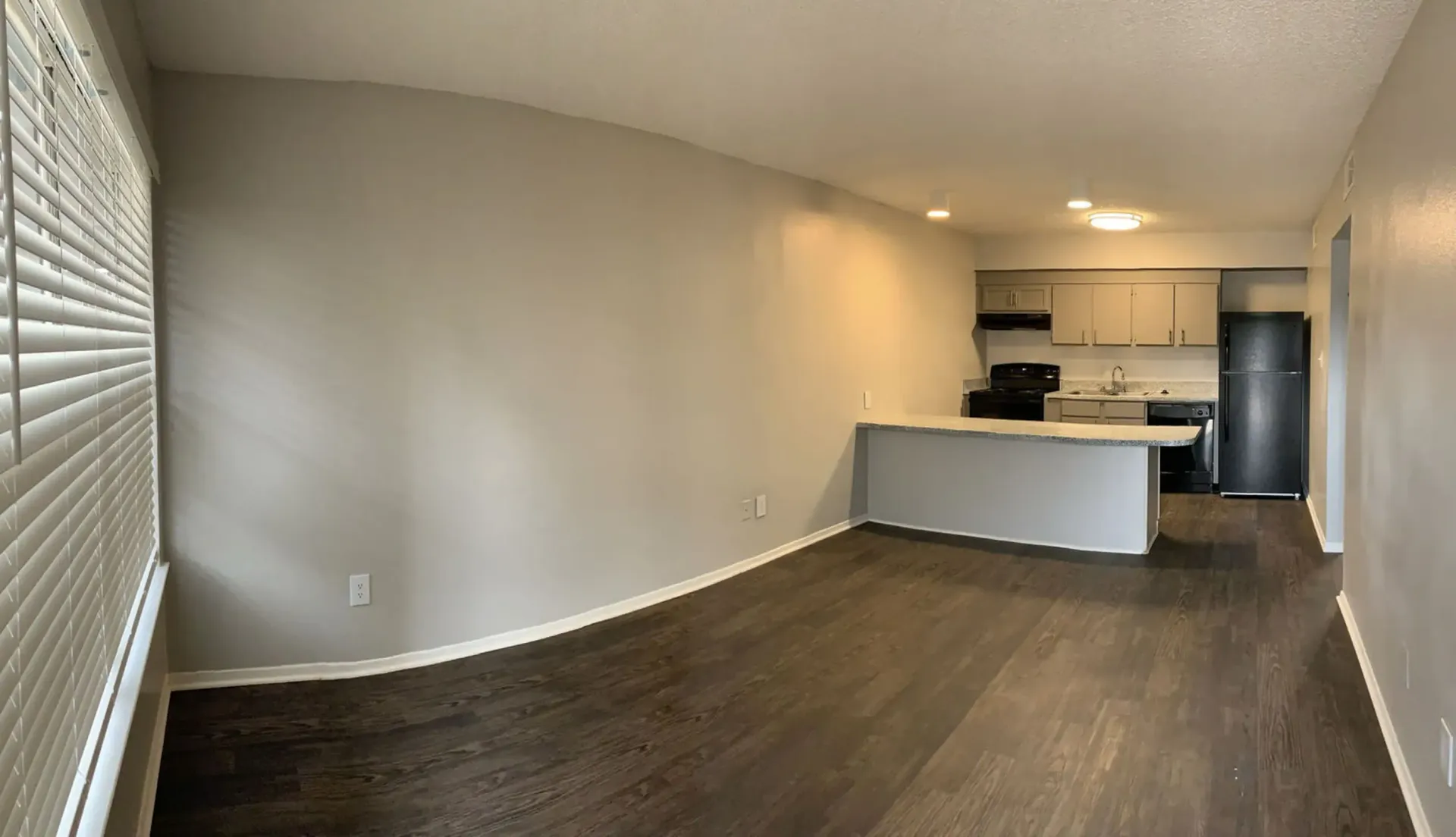 A living room with hardwood floors and a kitchen in the background.