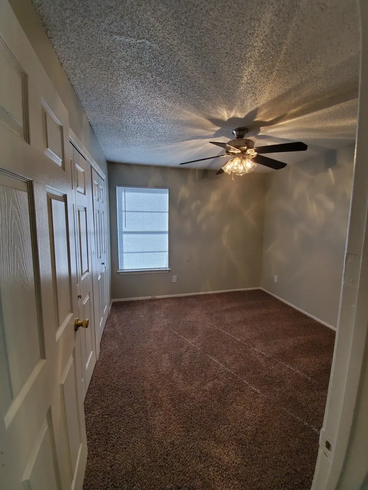 A bedroom with a ceiling fan and a window.