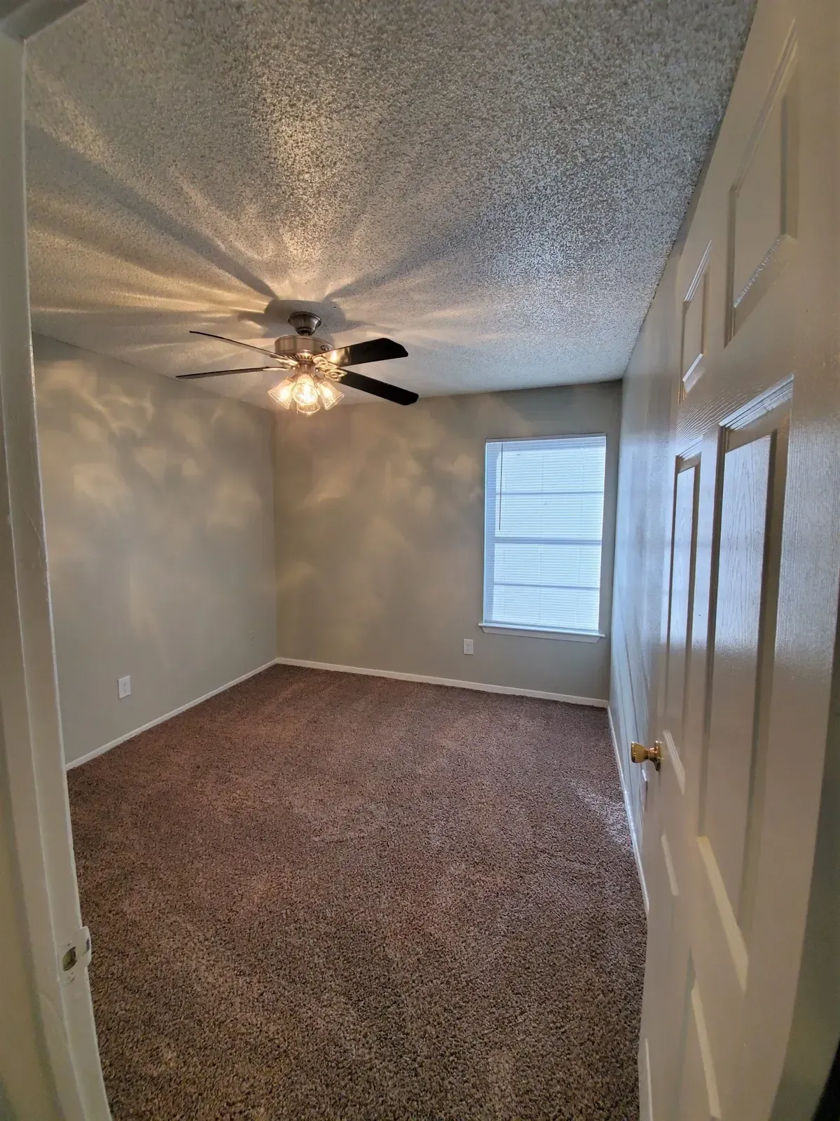 An empty bedroom with a ceiling fan and a window.