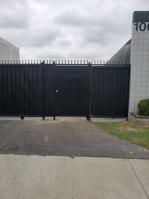 Black metal gate with spikes, leading to a building with the number 1060 on it. Cloudy sky above.