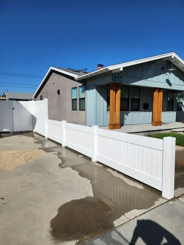 White fence surrounds a blue house with brown pillars. Clear blue sky overhead.
