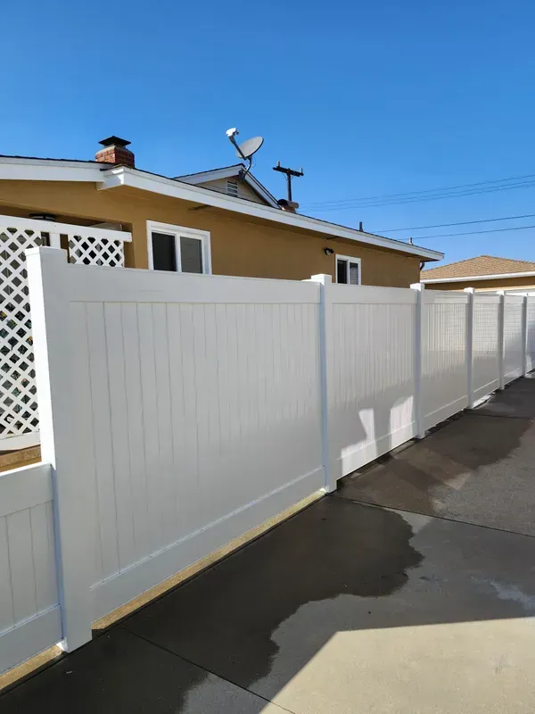 White vinyl fence in front of a tan house, under a clear blue sky.
