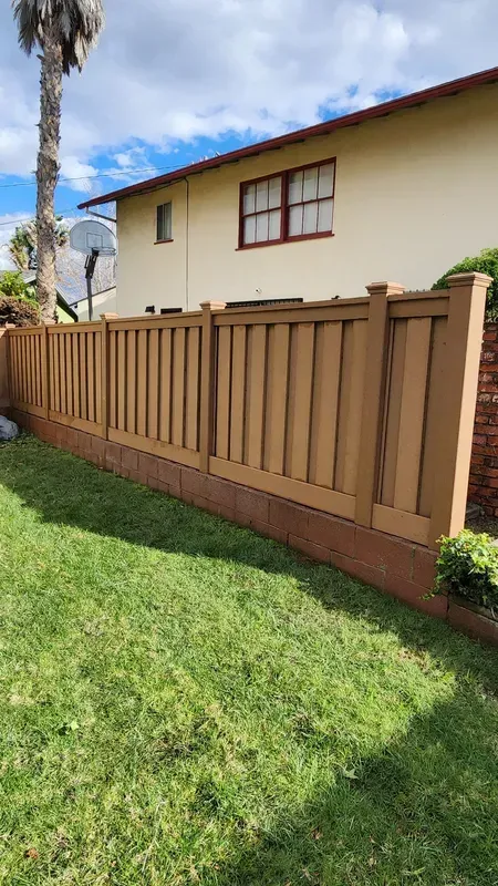 Brown fence in front of a yellow building and green grass under a blue sky.