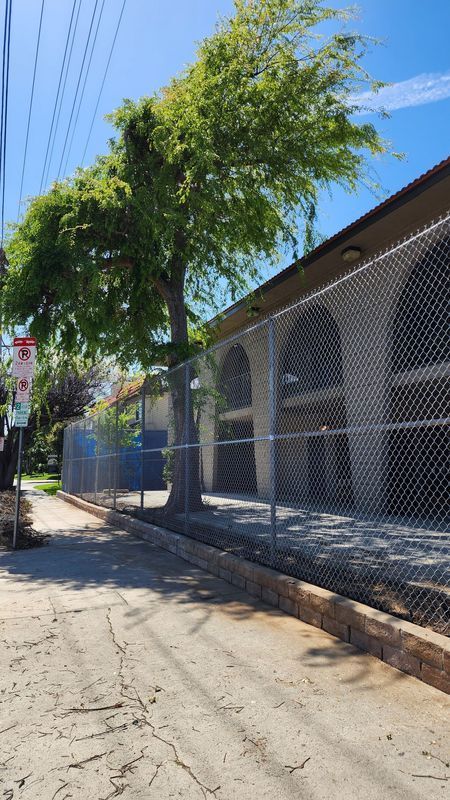 Fenced industrial area with chain-link fence, metal gate, razor wire, and asphalt road.