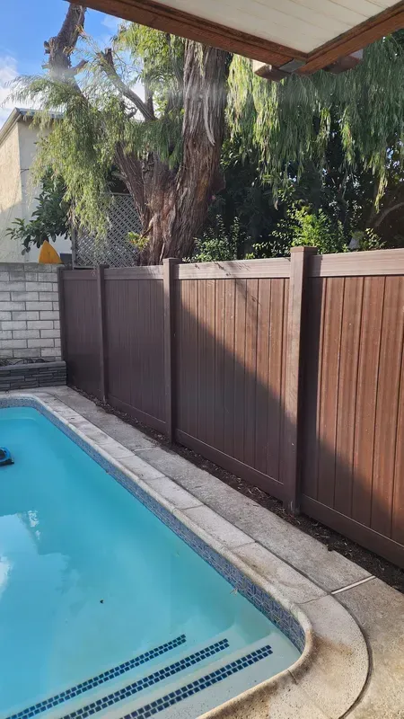 Swimming pool with brown privacy fence and a lush green tree in the background.