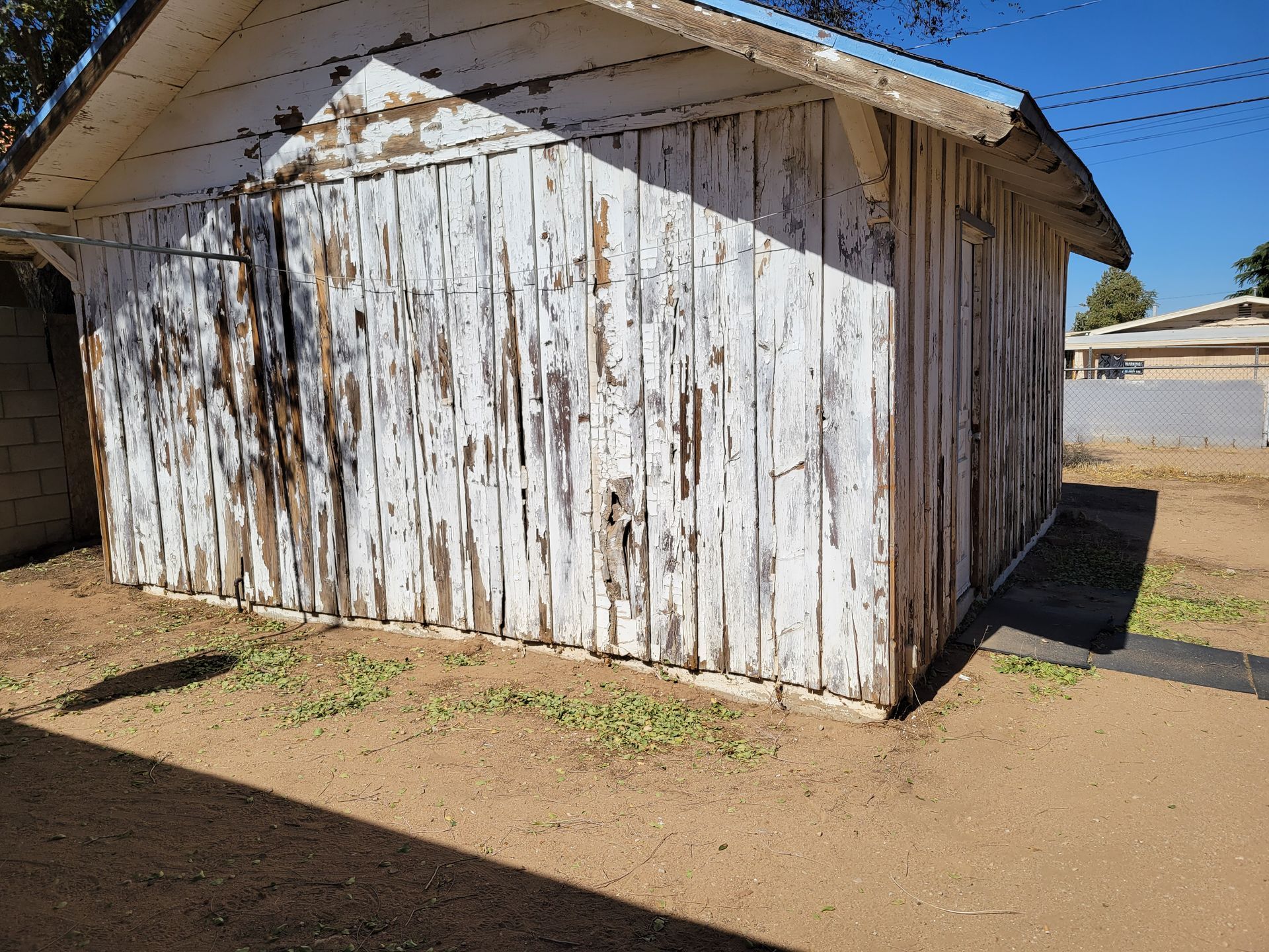 A white wooden shed is sitting in the middle of a dirt field.