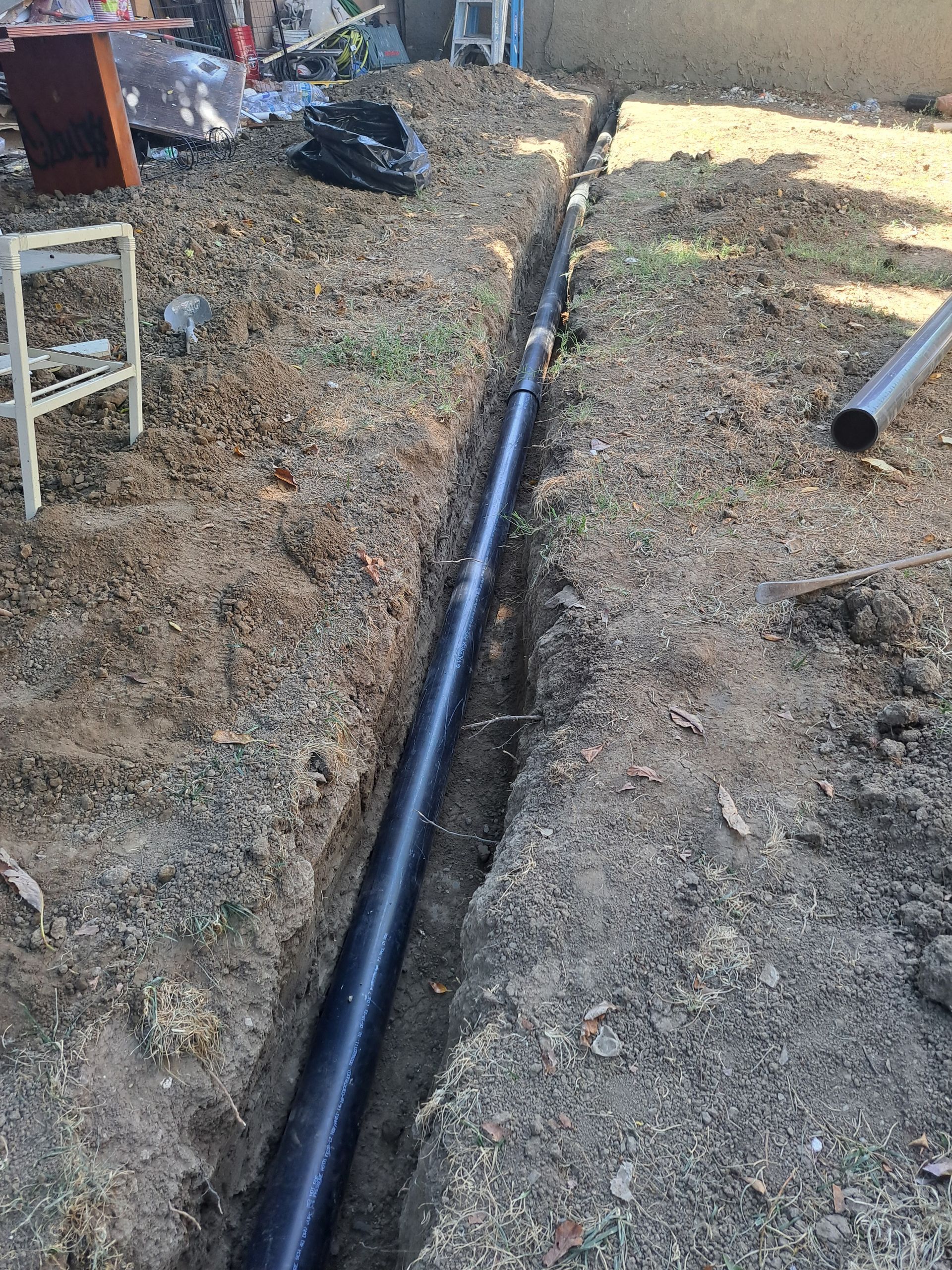 A black pipe is being installed in a trench in the dirt.