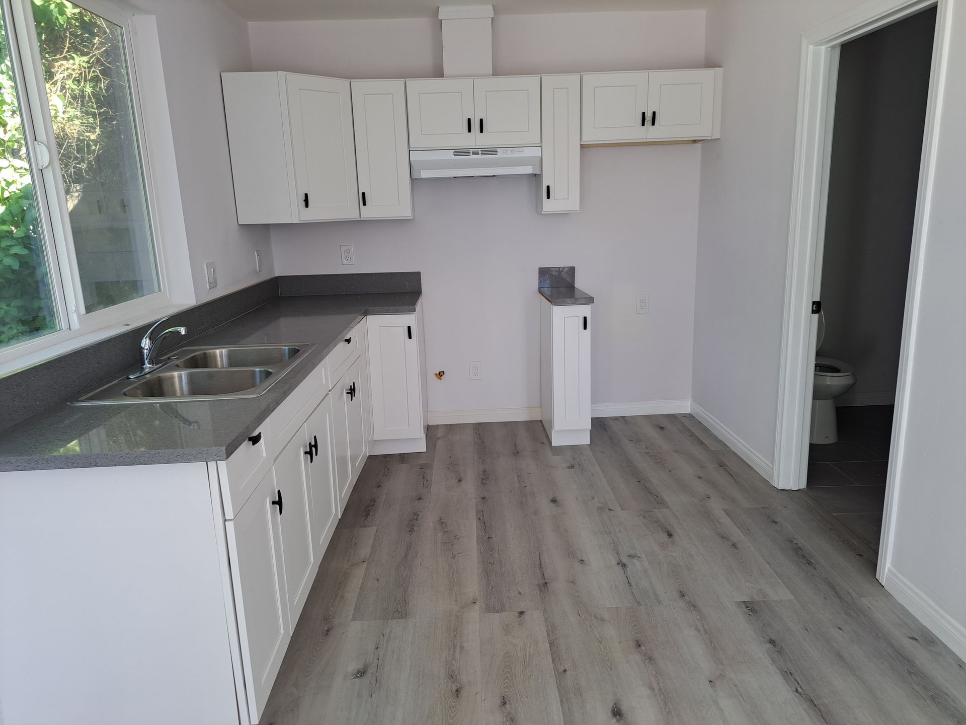 An empty kitchen with white cabinets and a sink.