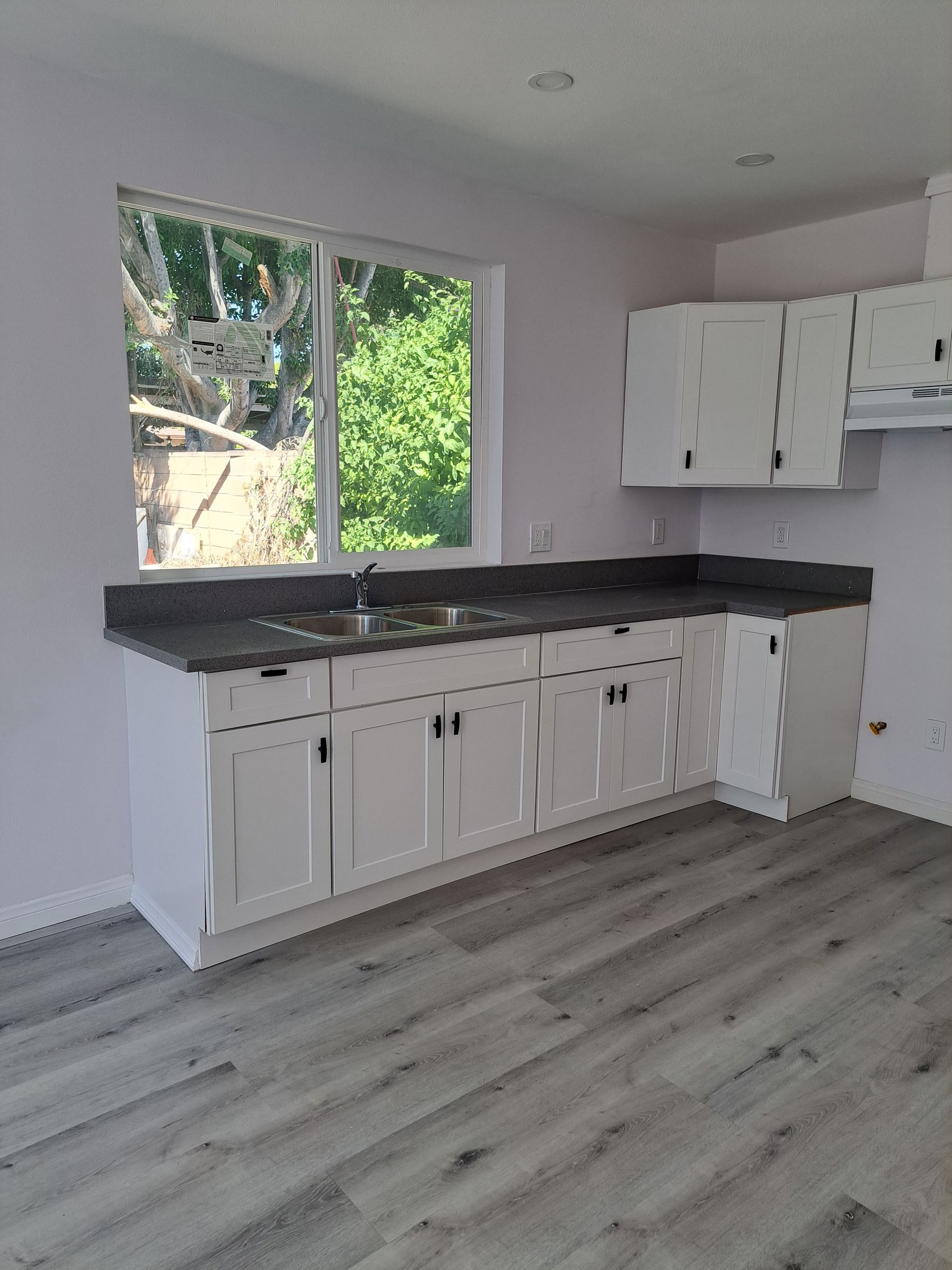 An empty kitchen with white cabinets and a large window