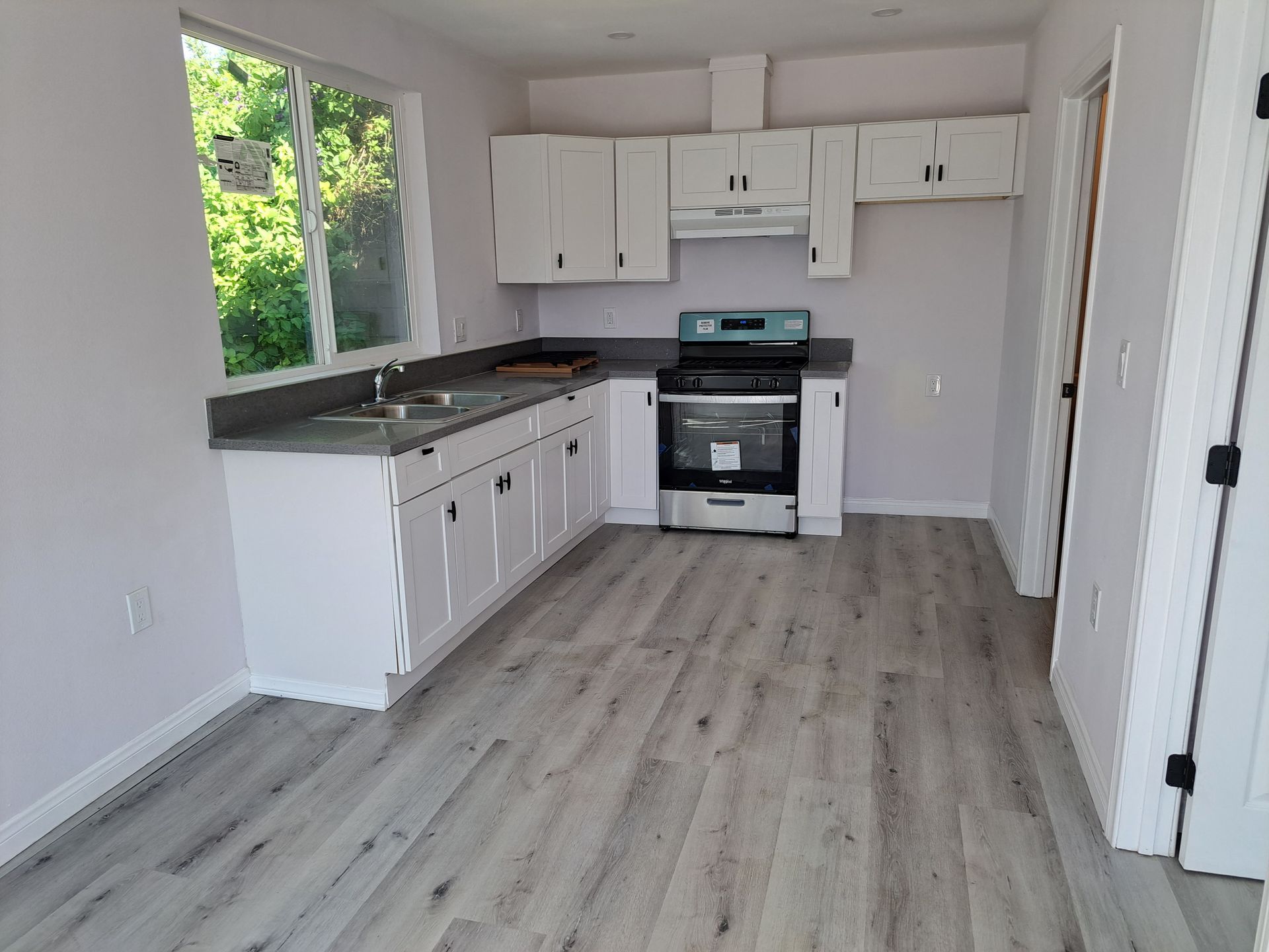 A kitchen with white cabinets , a stove , a sink and a window.