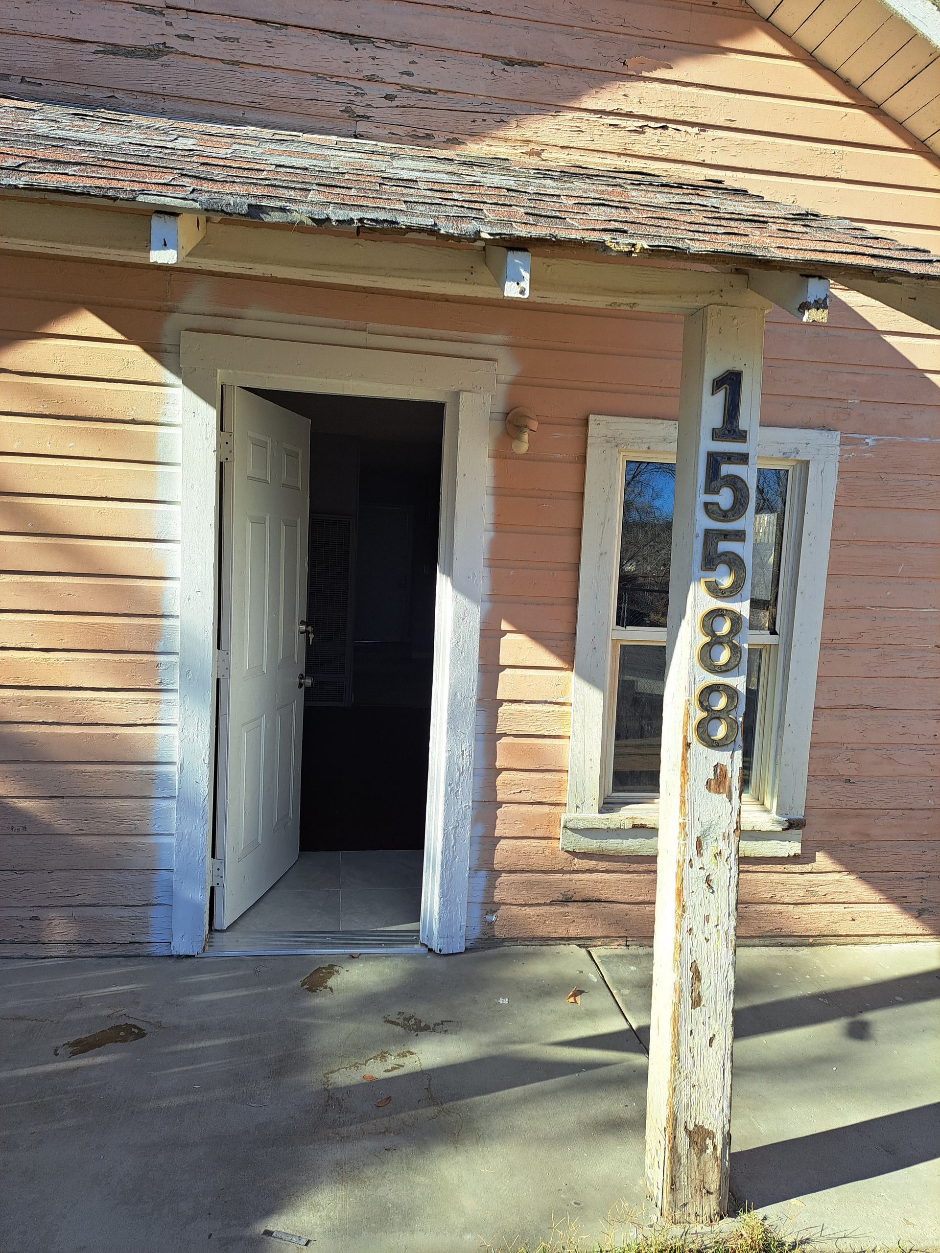 A brick building with the door open and a wooden post with the number 1 on it