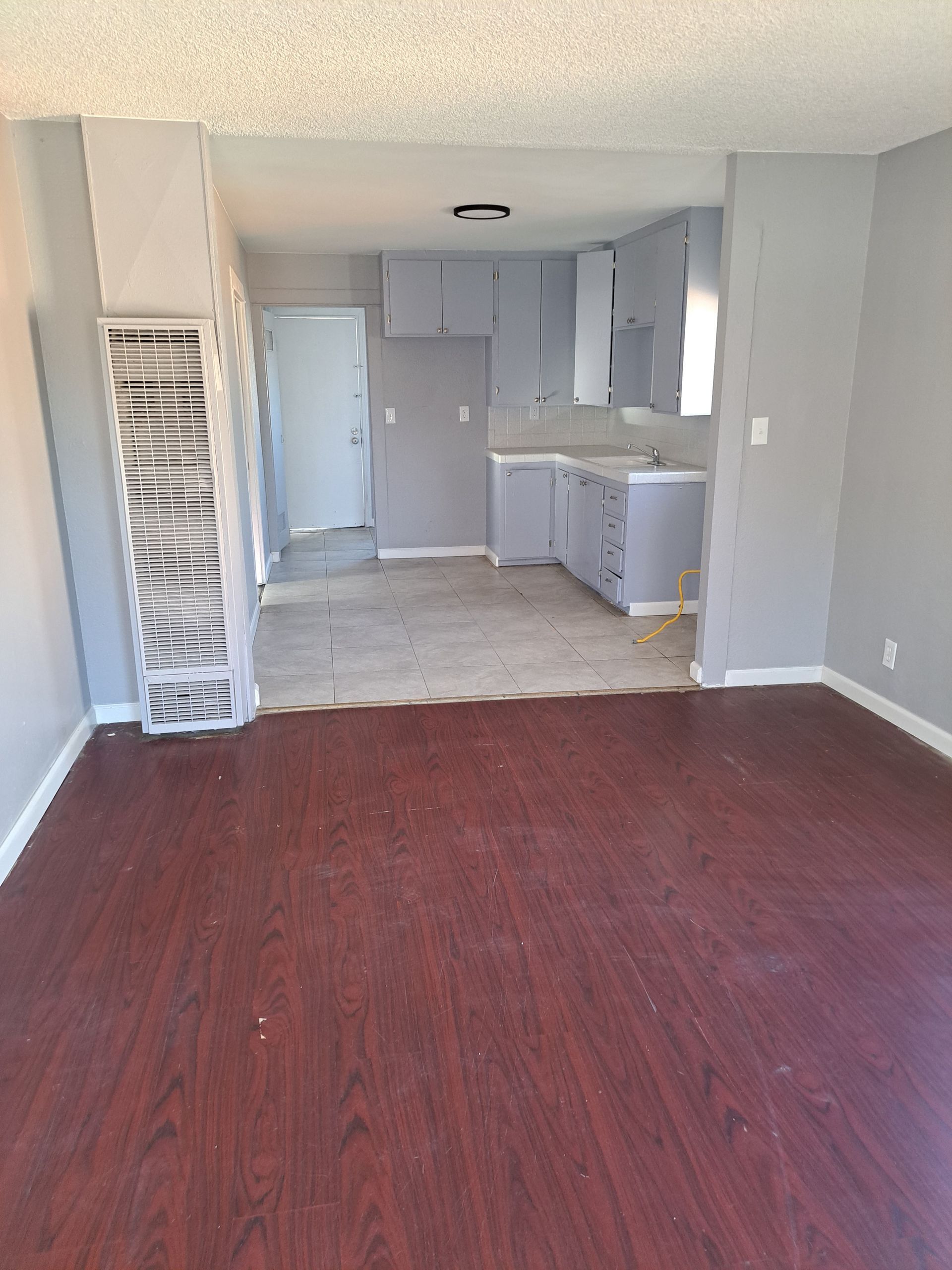 A living room with a wooden floor and a kitchen in the background.