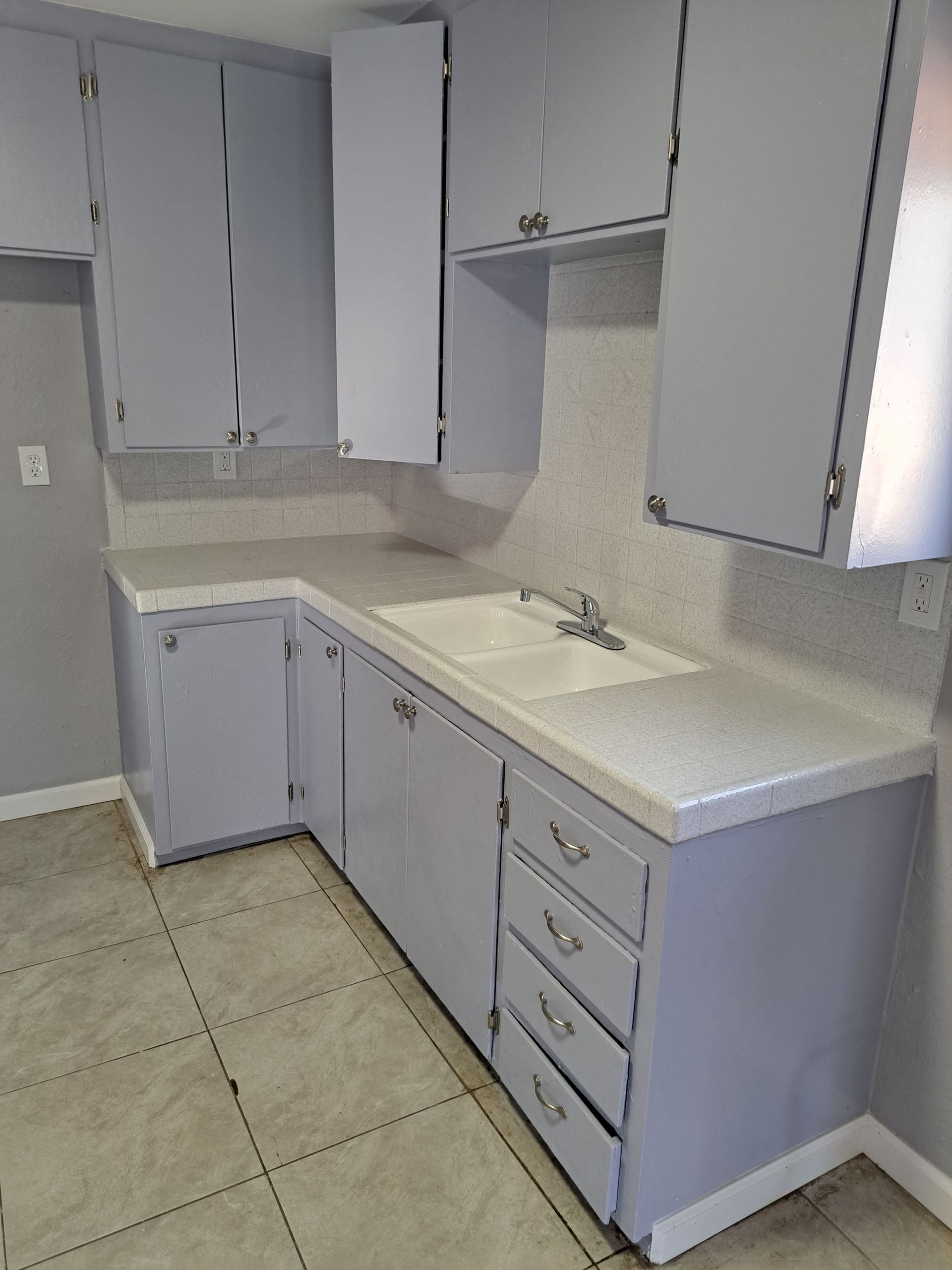 A kitchen with gray cabinets , a sink , and a stove.