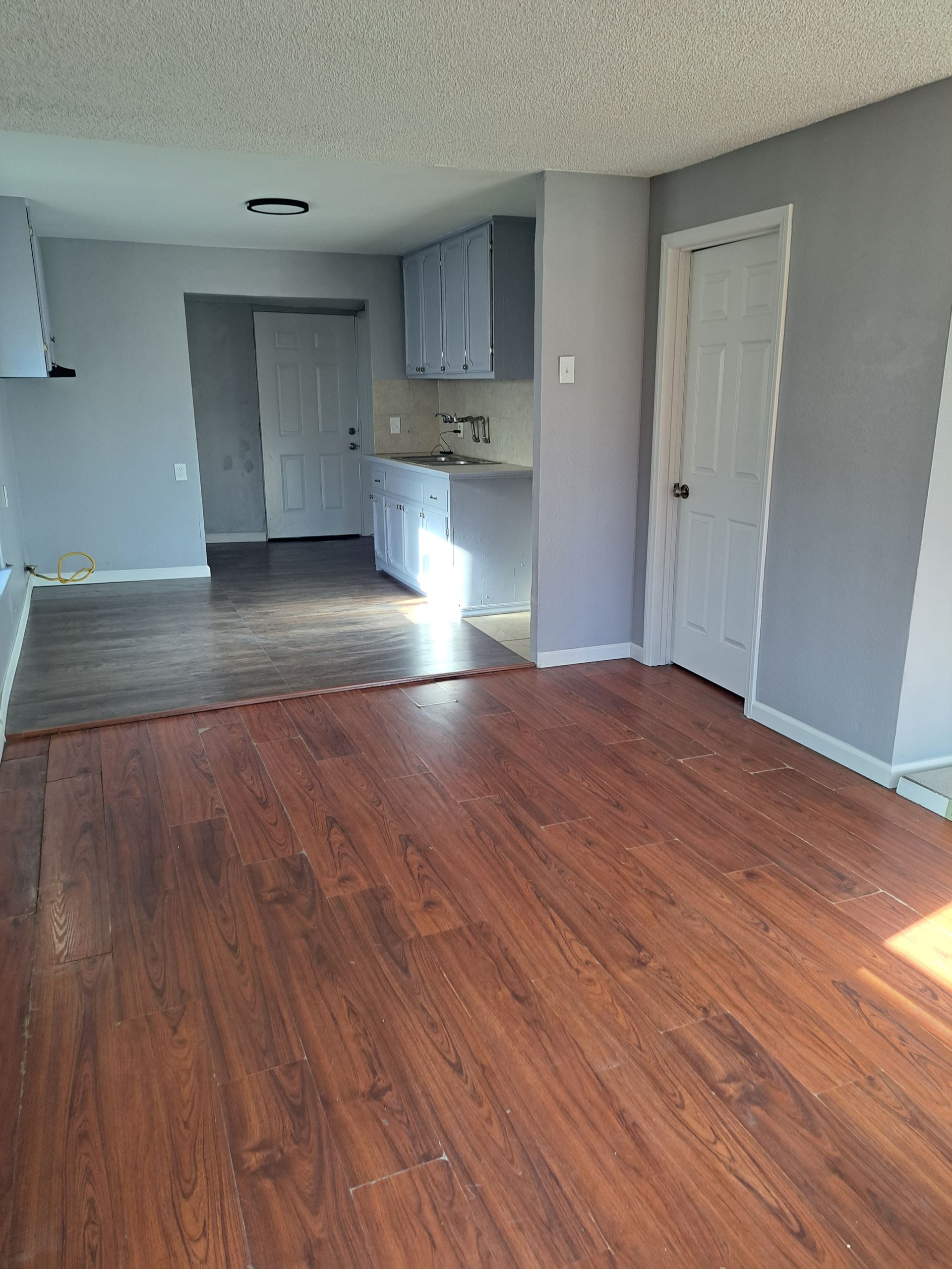 A living room with hardwood floors and a kitchen in the background.