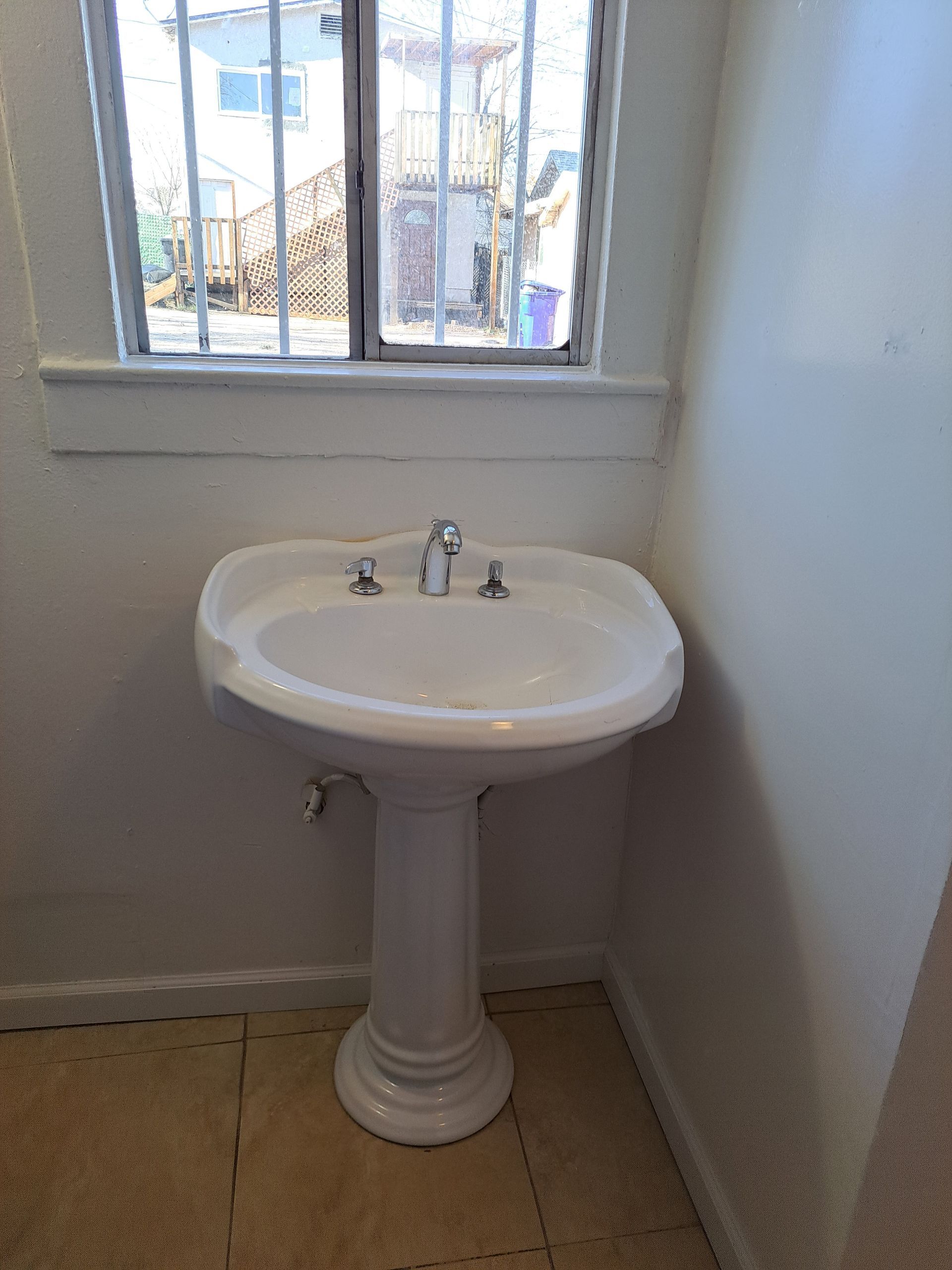 A white pedestal sink in a bathroom next to a window