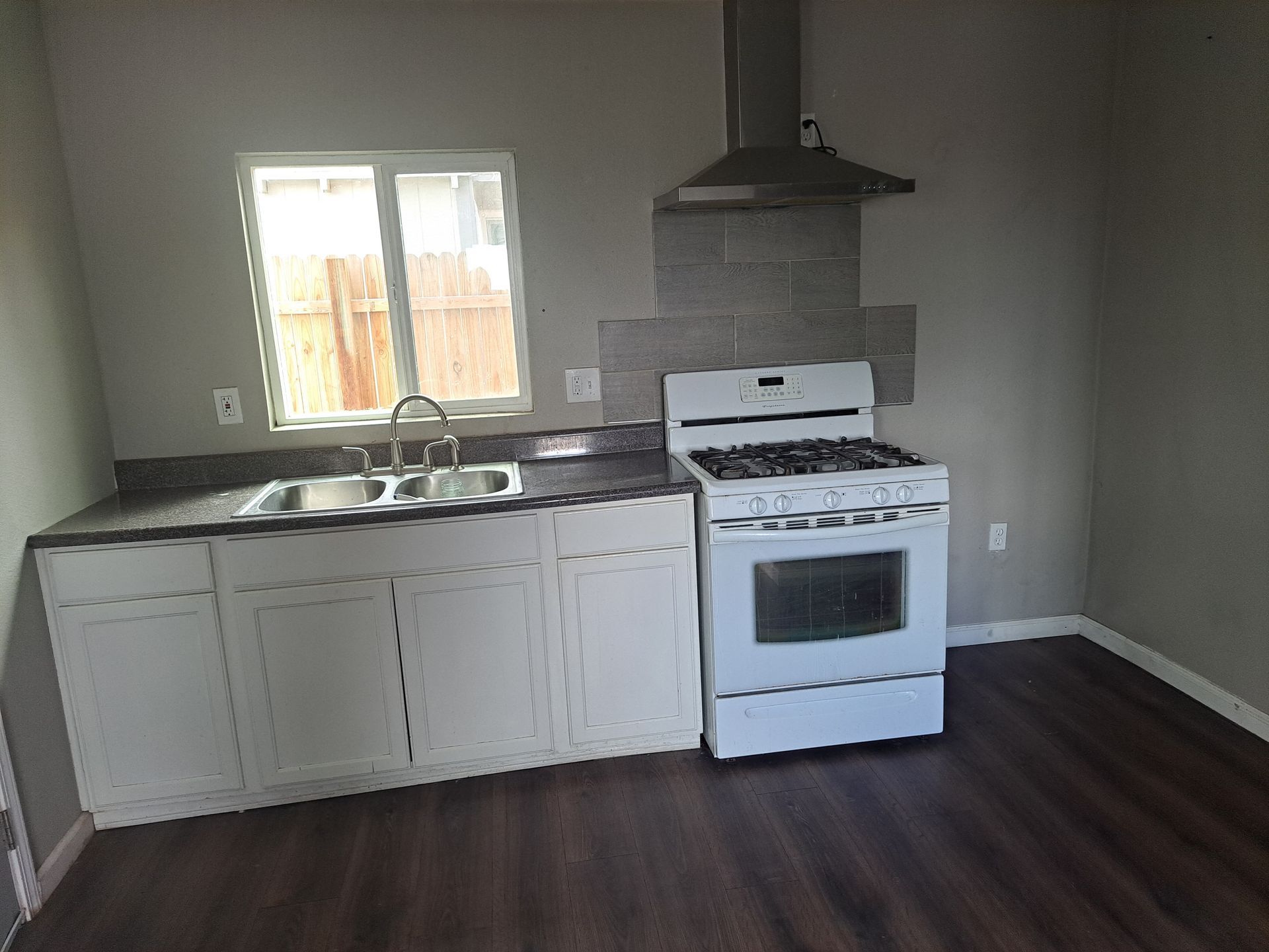 An empty kitchen with a stove , sink , and window.