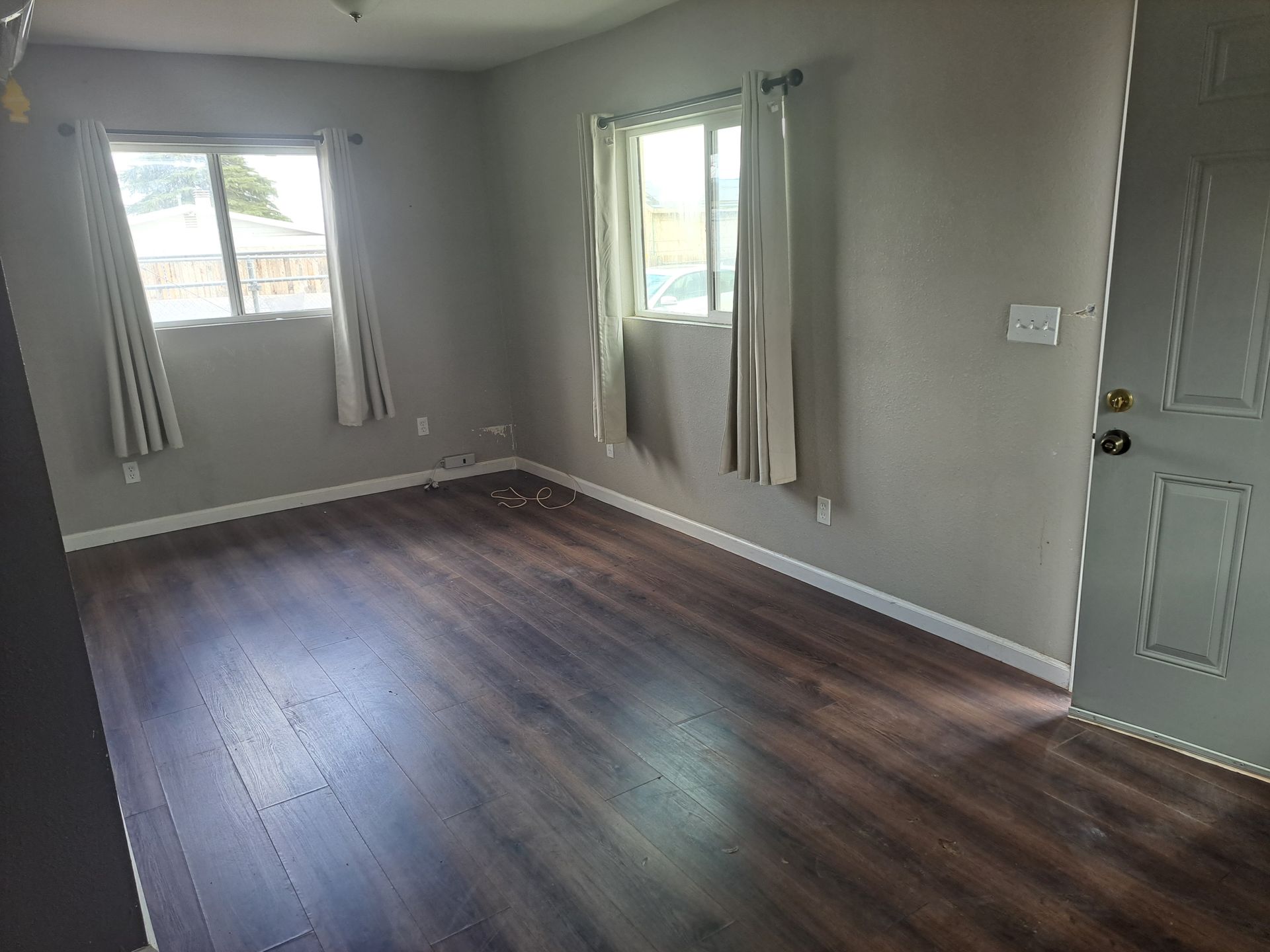 A living room with hardwood floors , two windows and a door.