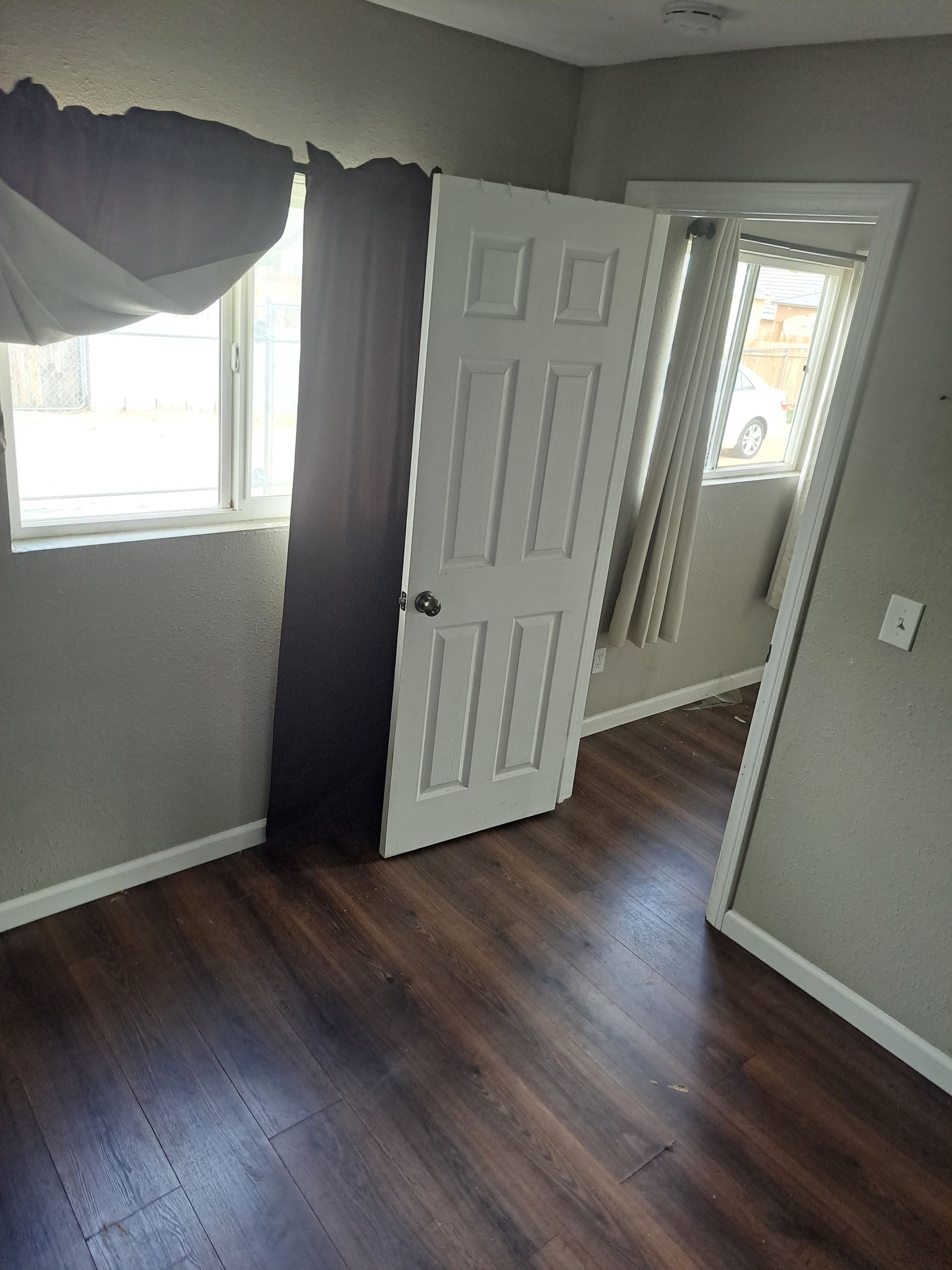 A bedroom with hardwood floors , a window and a door.