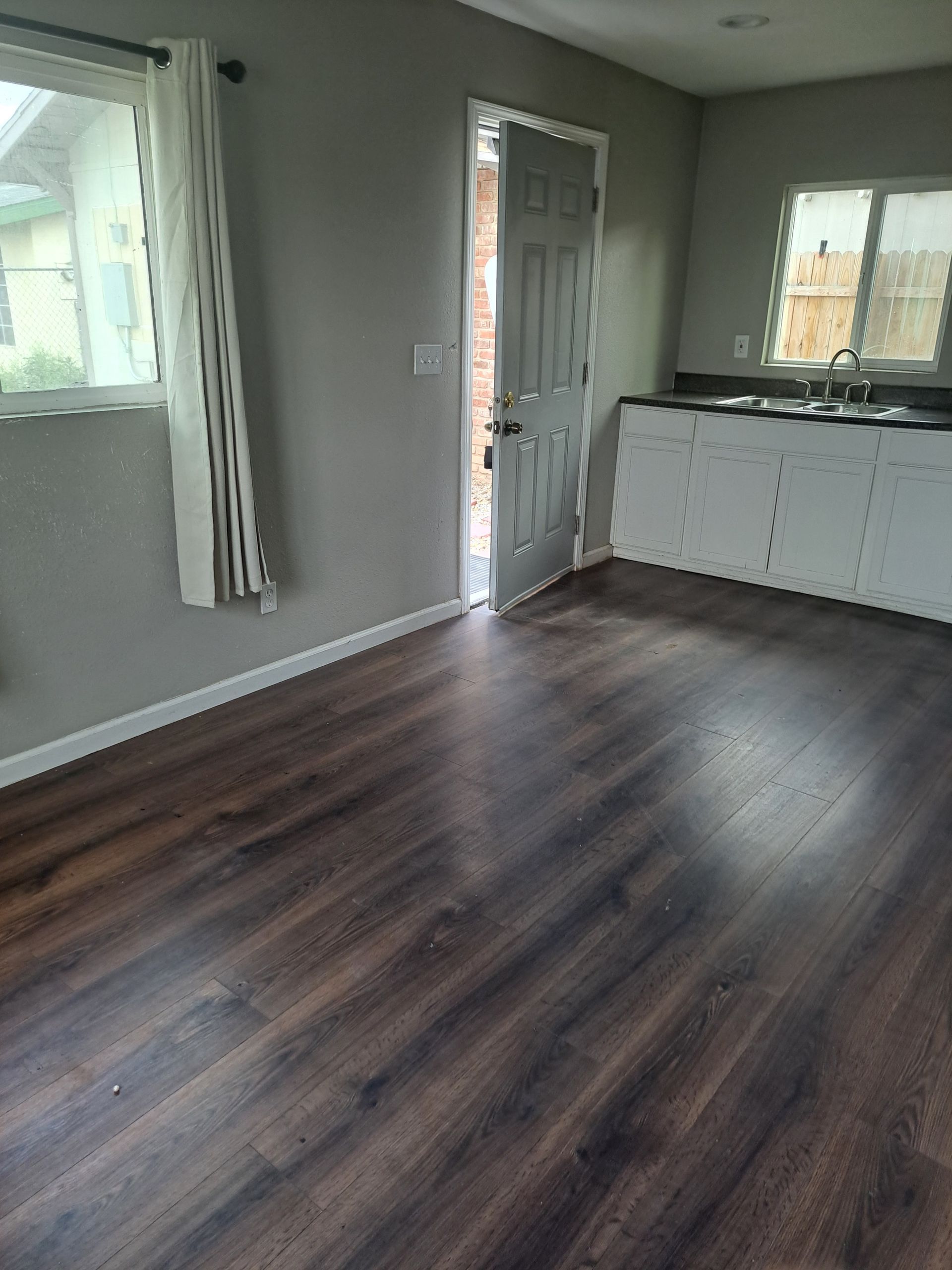 A living room with hardwood floors and a kitchen in the background.