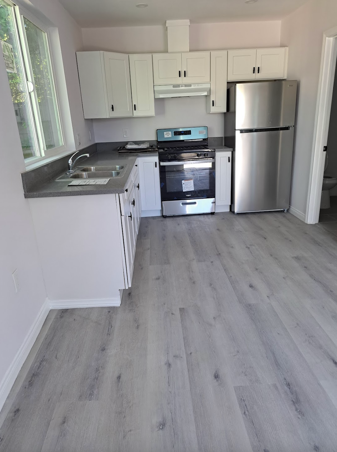 A kitchen with a stove , refrigerator , sink and window.