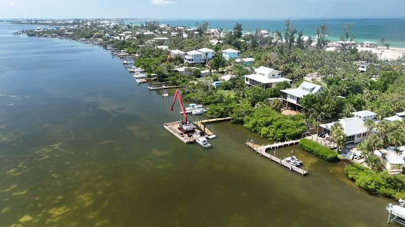Aerial view of a coastal neighborhood with a marina, docks, and green shoreline beside calm water