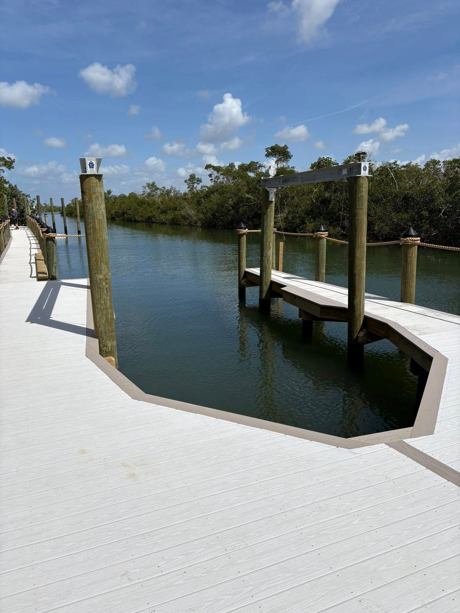 Bright waterfront dock with white walkway, wooden posts, and calm blue water under a sunny sky