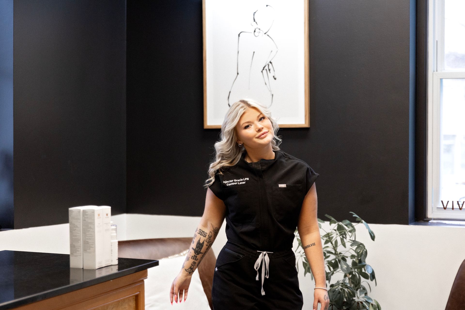 A woman in a black scrub suit is standing in a room.