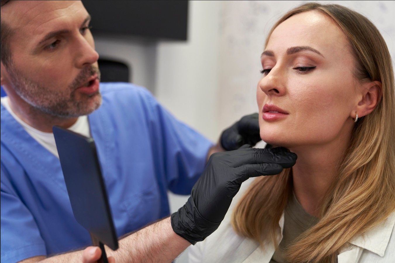 A doctor is examining a woman 's neck with a mirror.