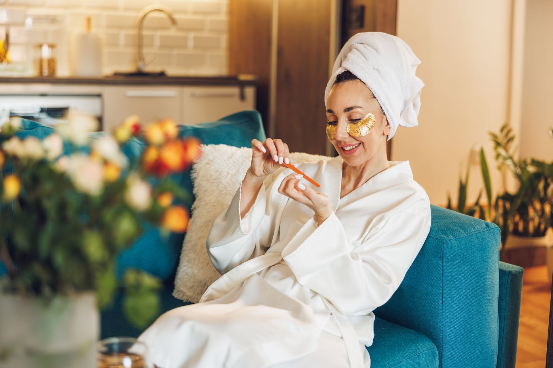 A woman in a bathrobe is sitting on a couch with a towel wrapped around her head.