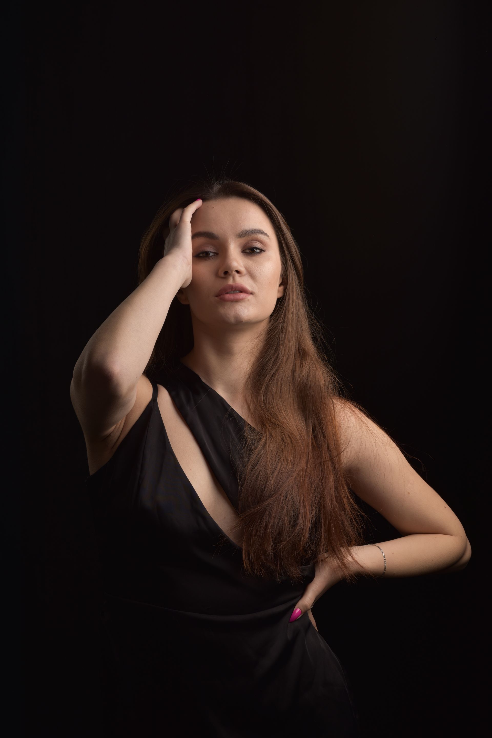 A woman in a black dress is standing in front of a black background.