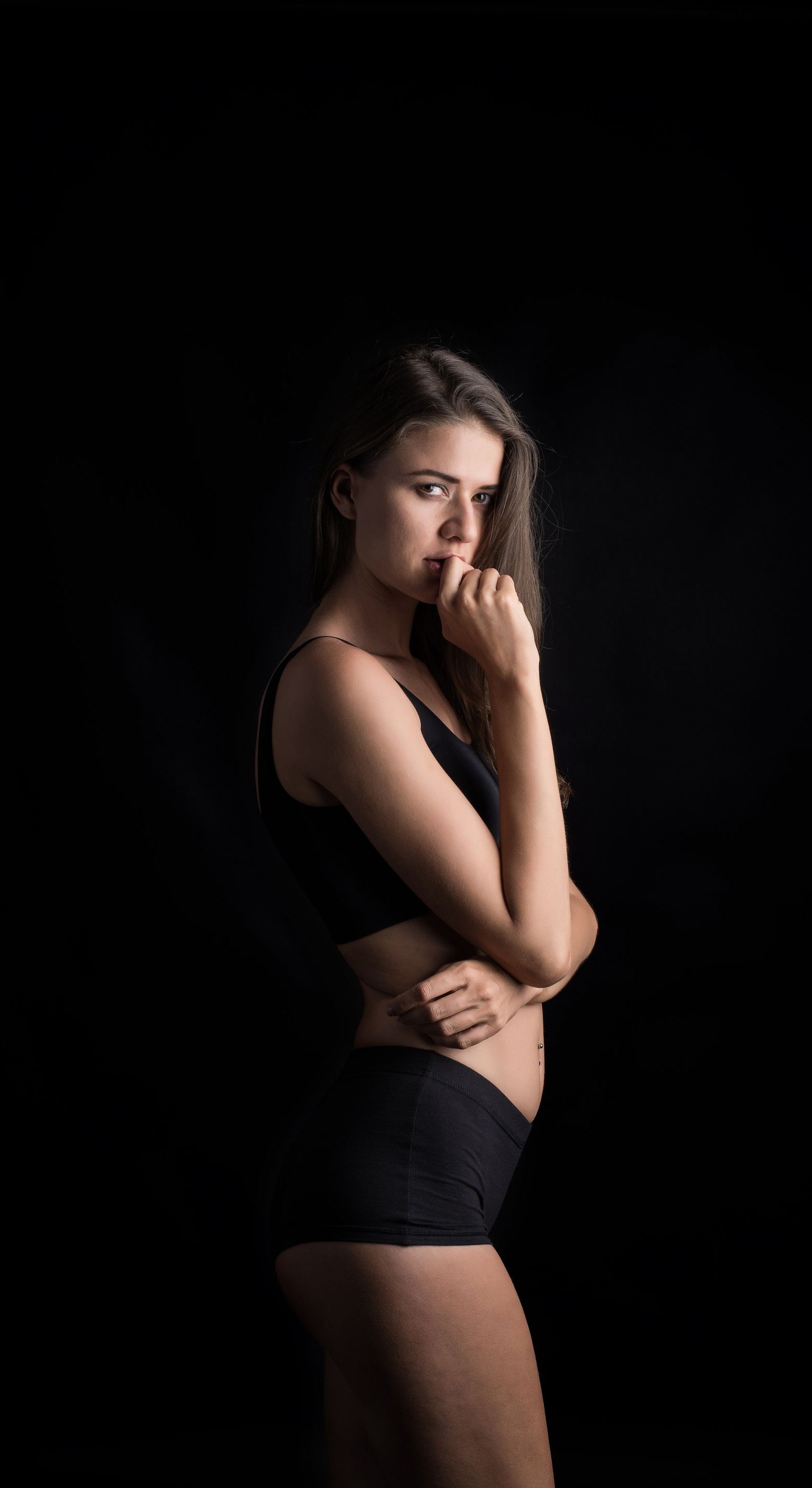 A woman in black underwear is standing in front of a black background.