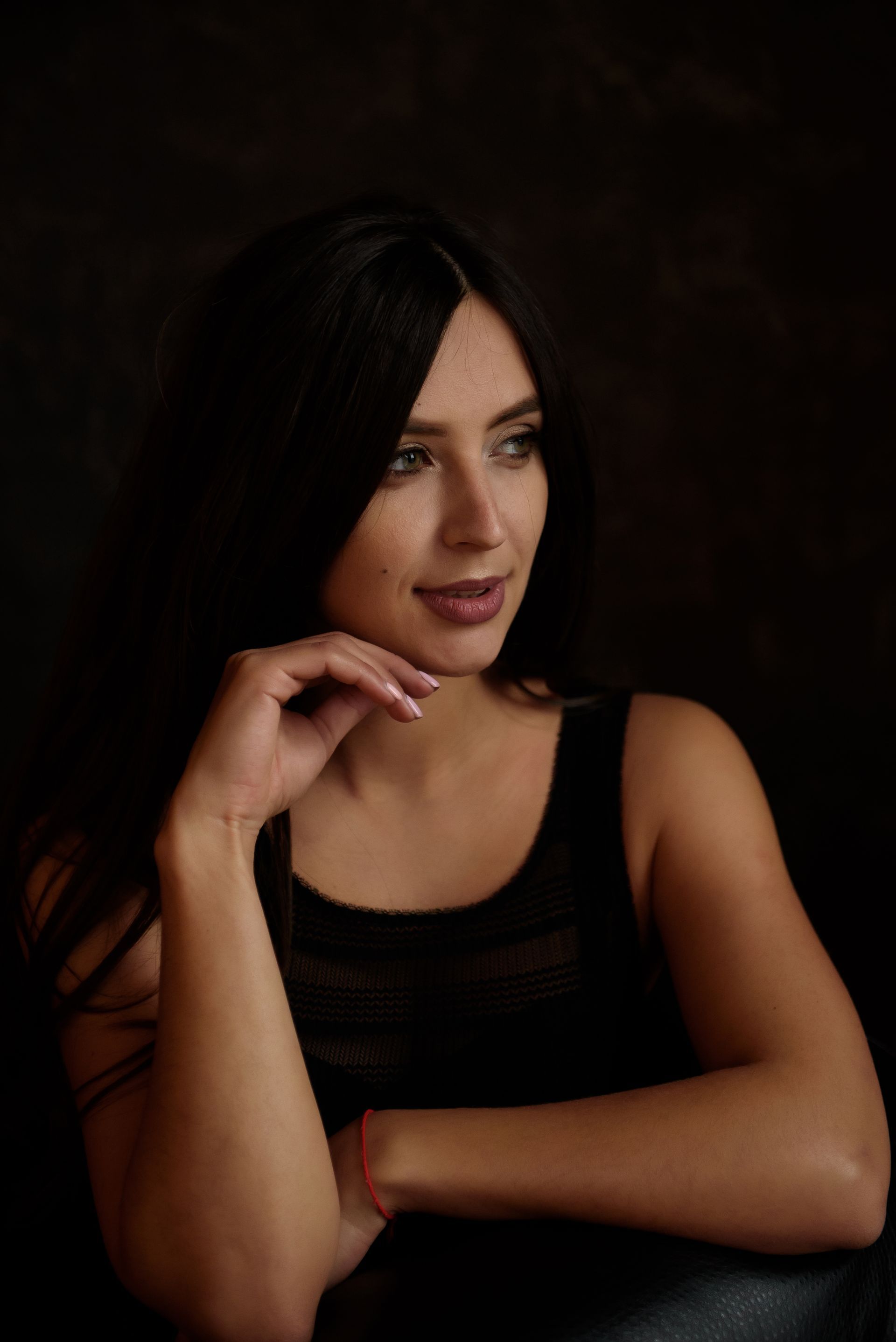 A woman in a black tank top is sitting in a chair with her hand on her chin.