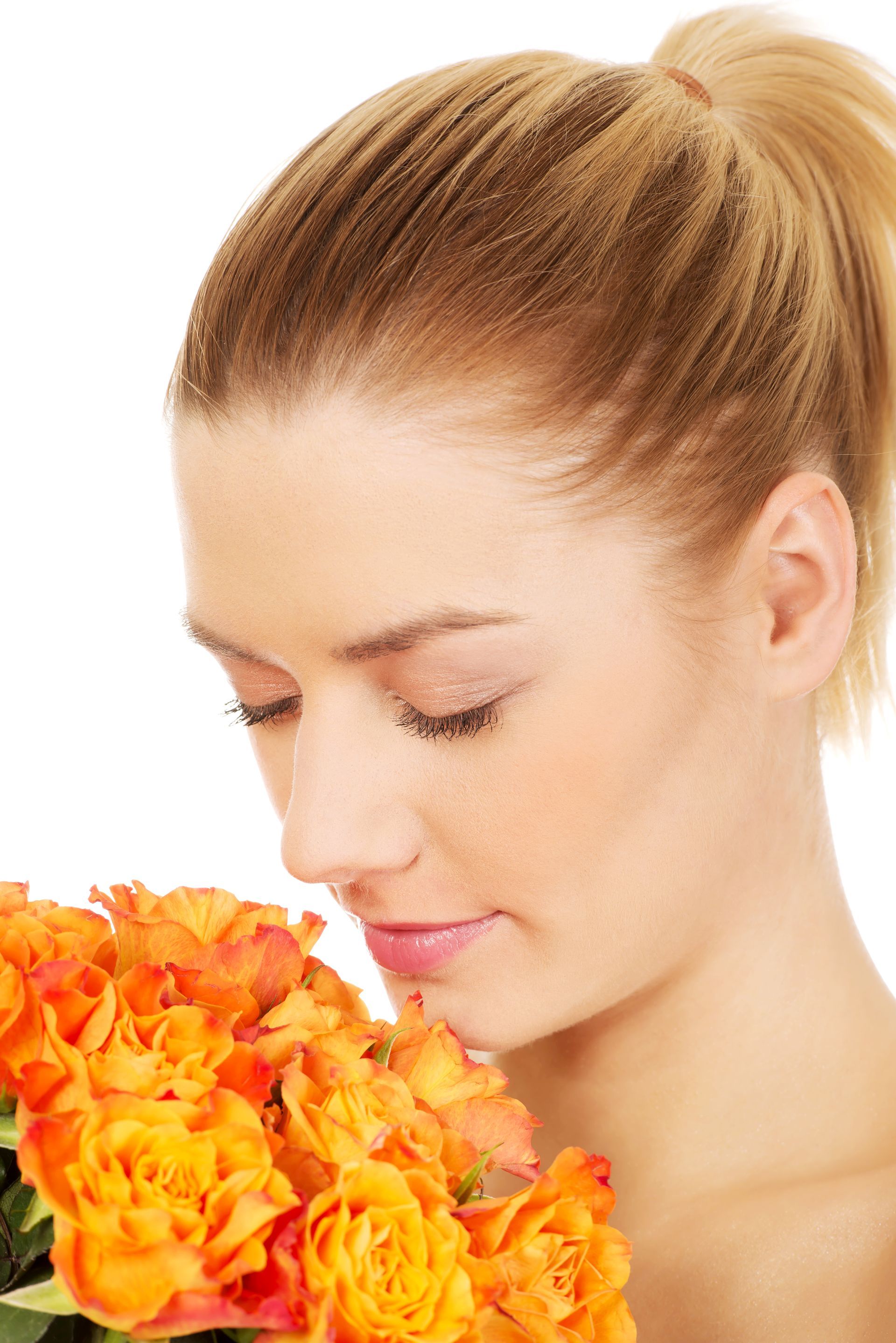 A woman is smelling a bouquet of orange roses.