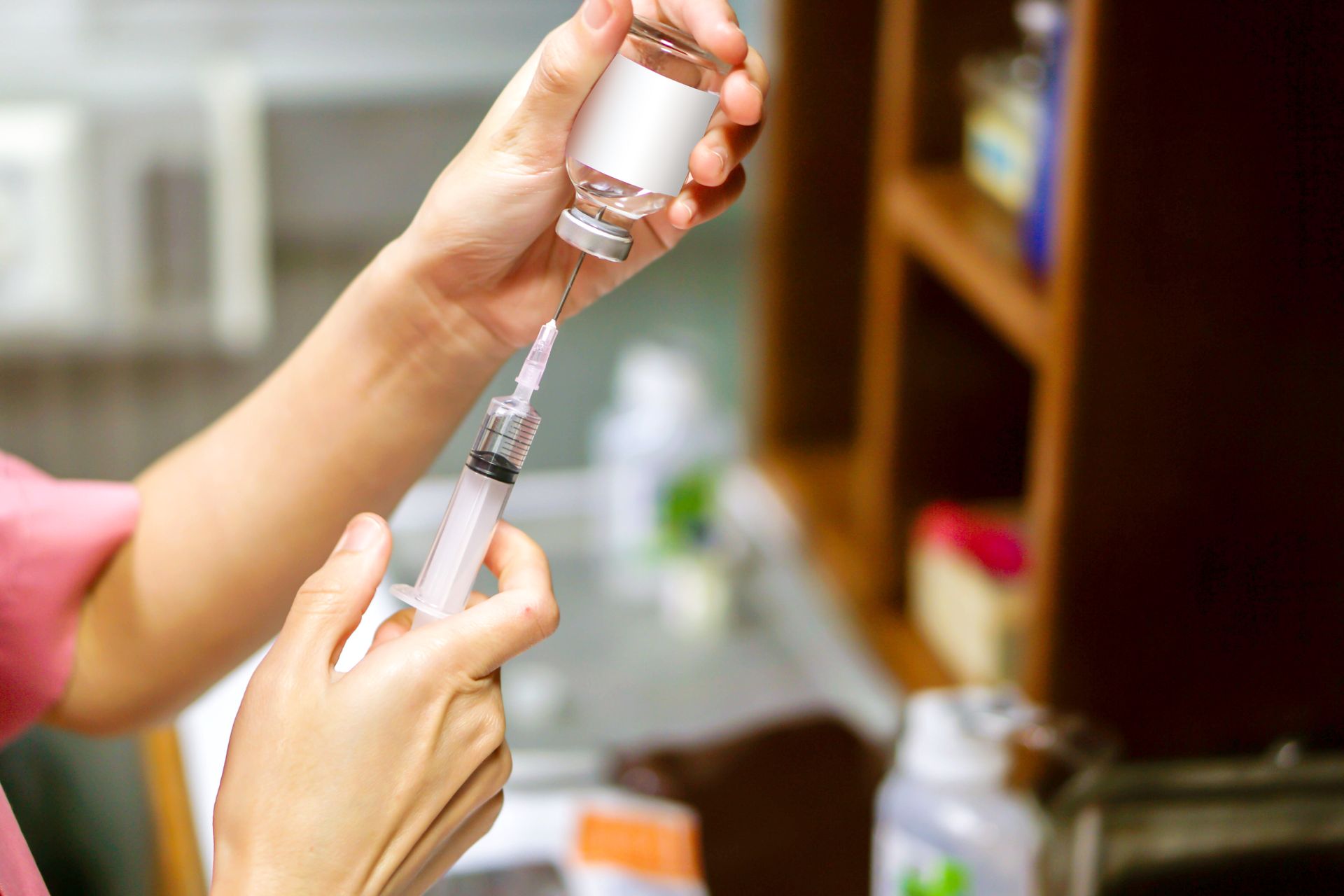 Close-up of a nurse or medical professional drawing liquid from a vial into a syringe.