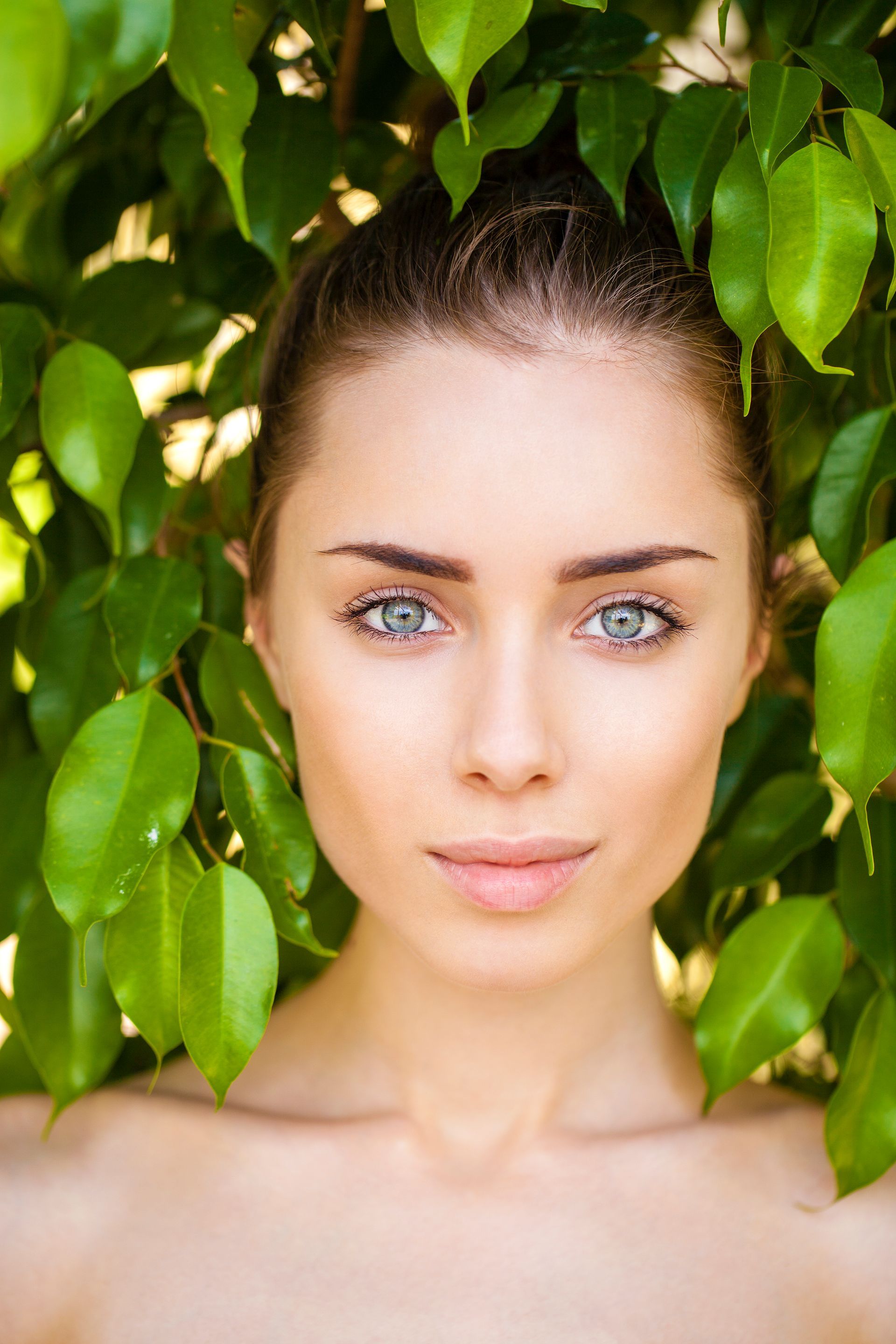 A close up of a woman 's face surrounded by green leaves.