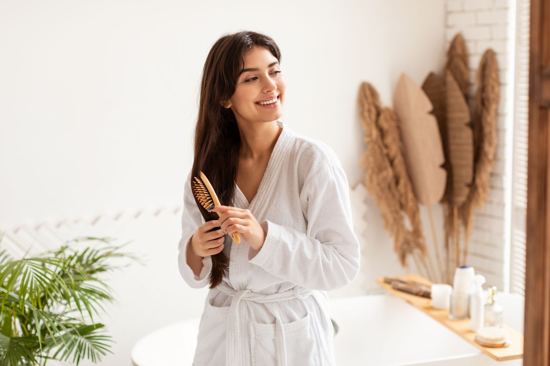 A woman in a bathrobe is brushing her hair in a bathroom.