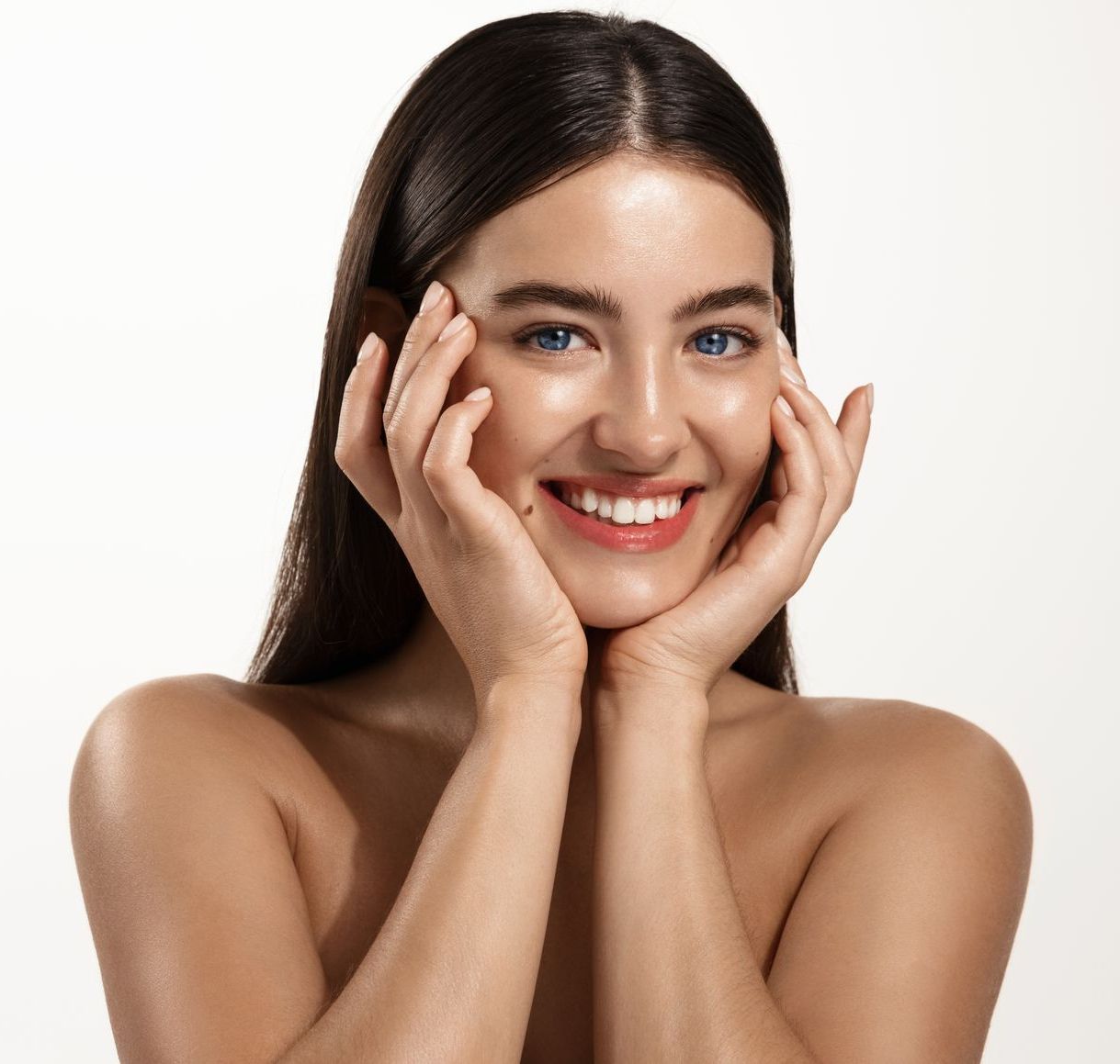 A woman is smiling and touching her face with her hands.