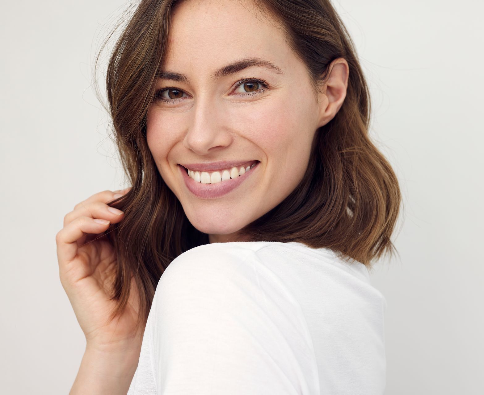 A woman in a white shirt is smiling and looking over her shoulder.