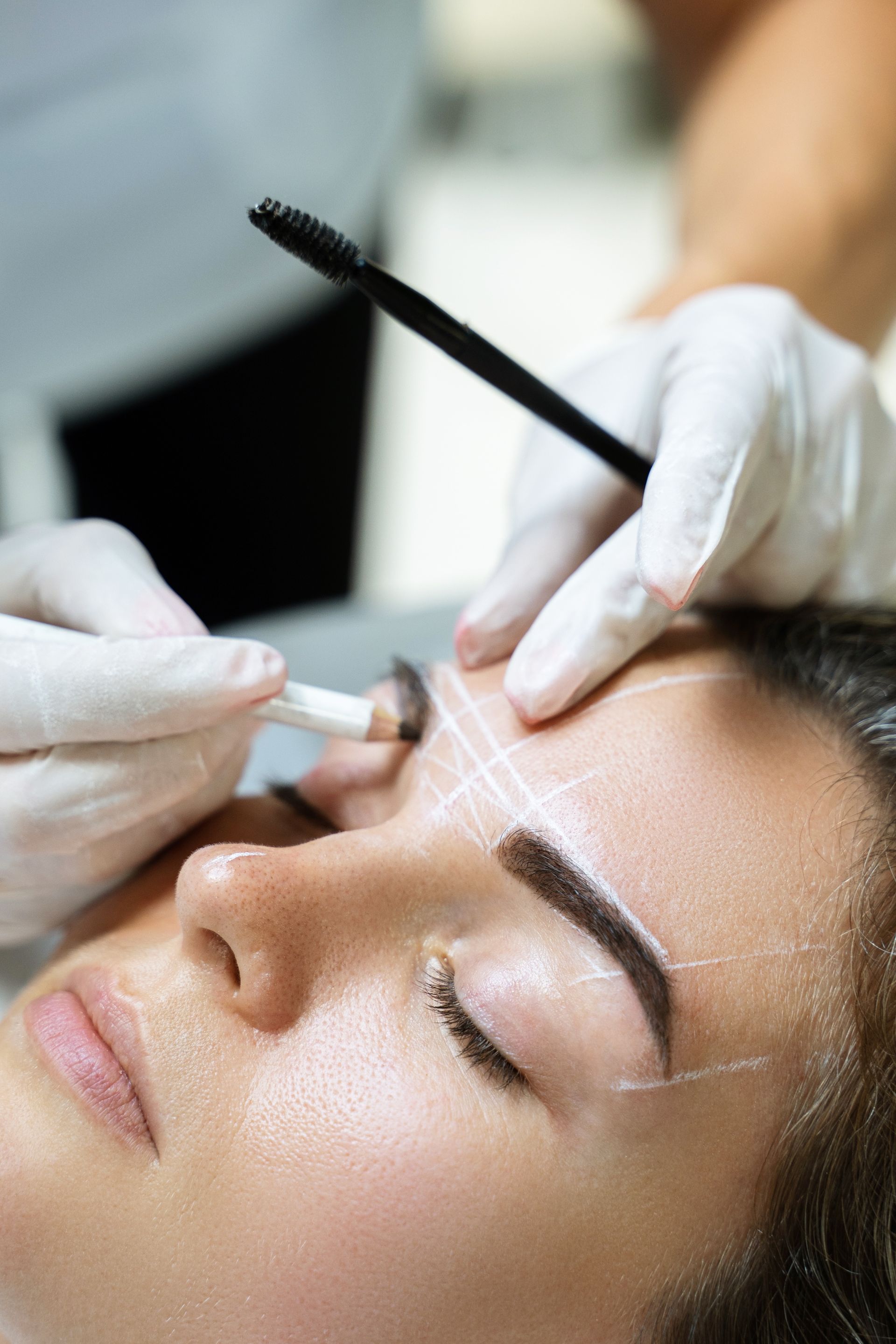 A woman is getting her eyebrows drawn by a tattoo artist.