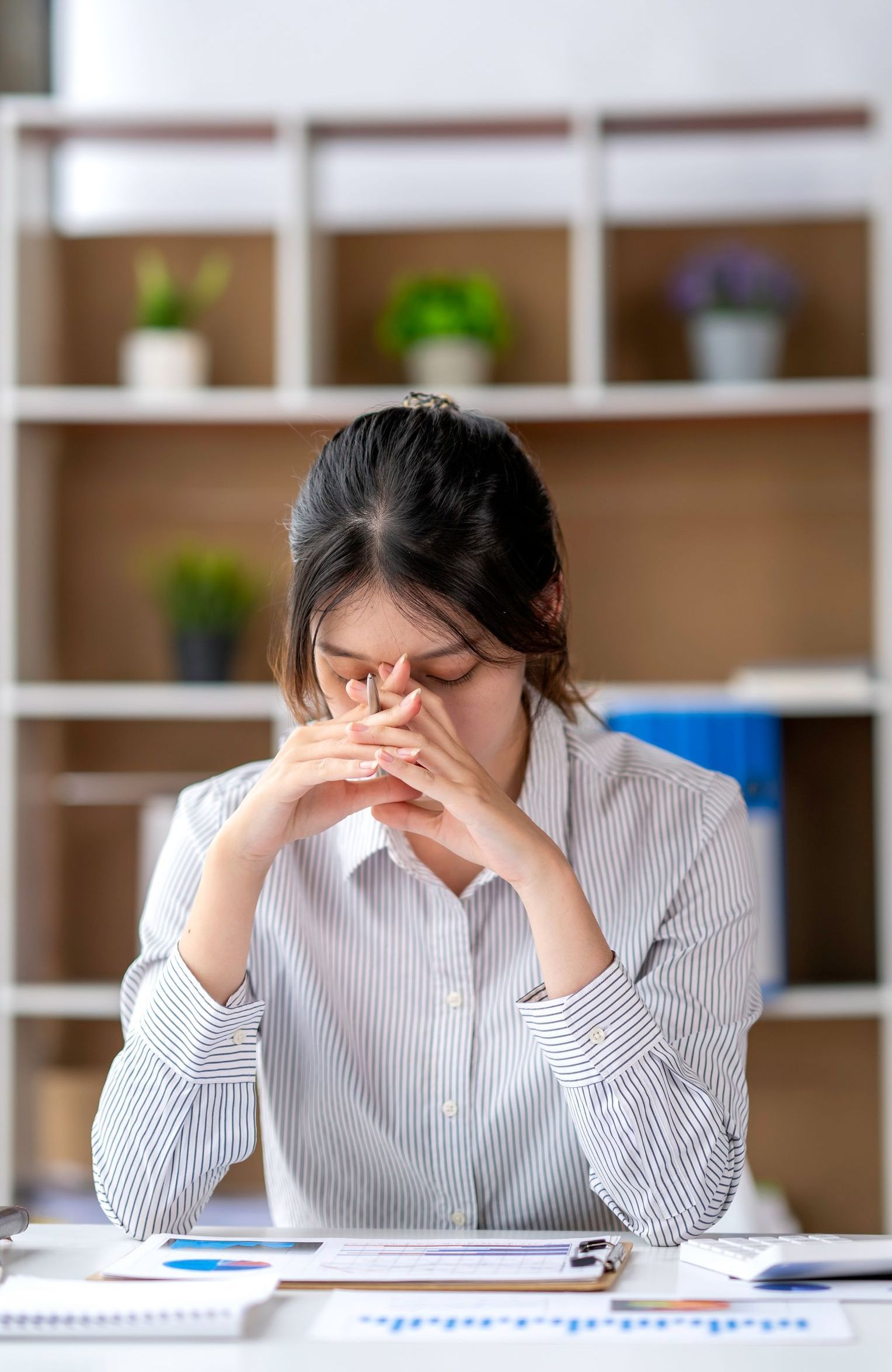 A woman is sitting at a desk with her hands on her face.