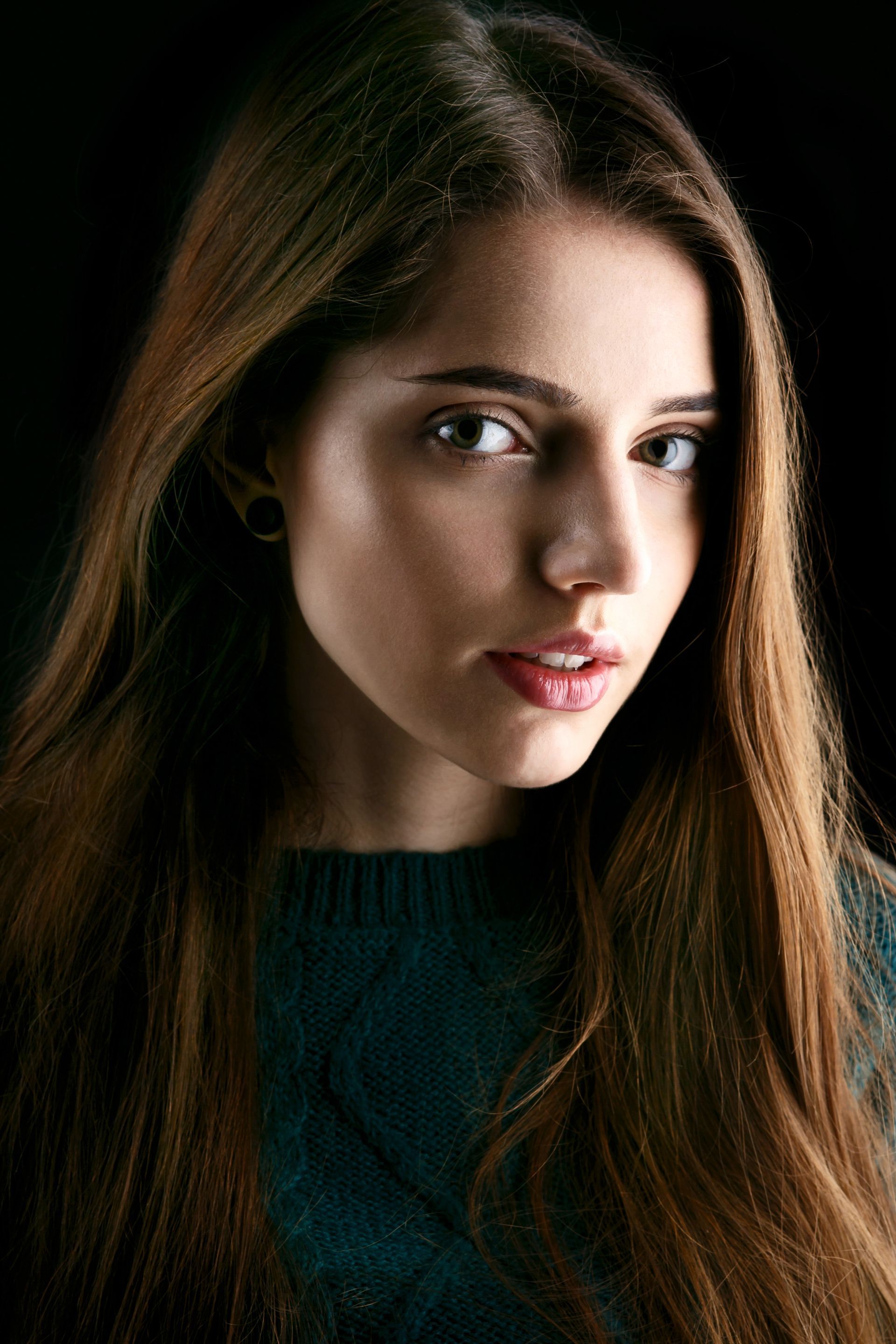 A young woman with long hair is wearing a green sweater and looking at the camera.