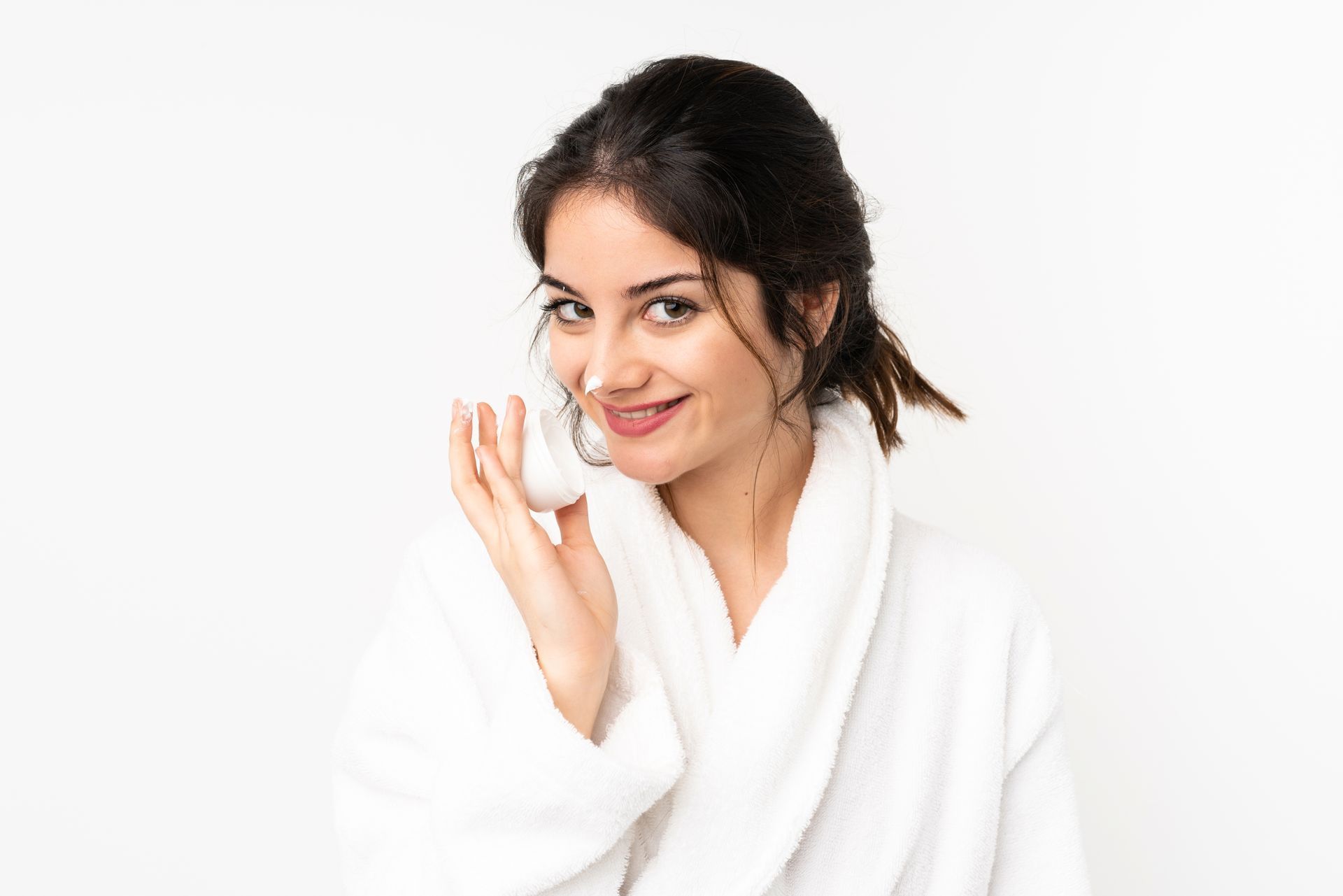 A woman in a bathrobe is cleaning her face with a sponge.