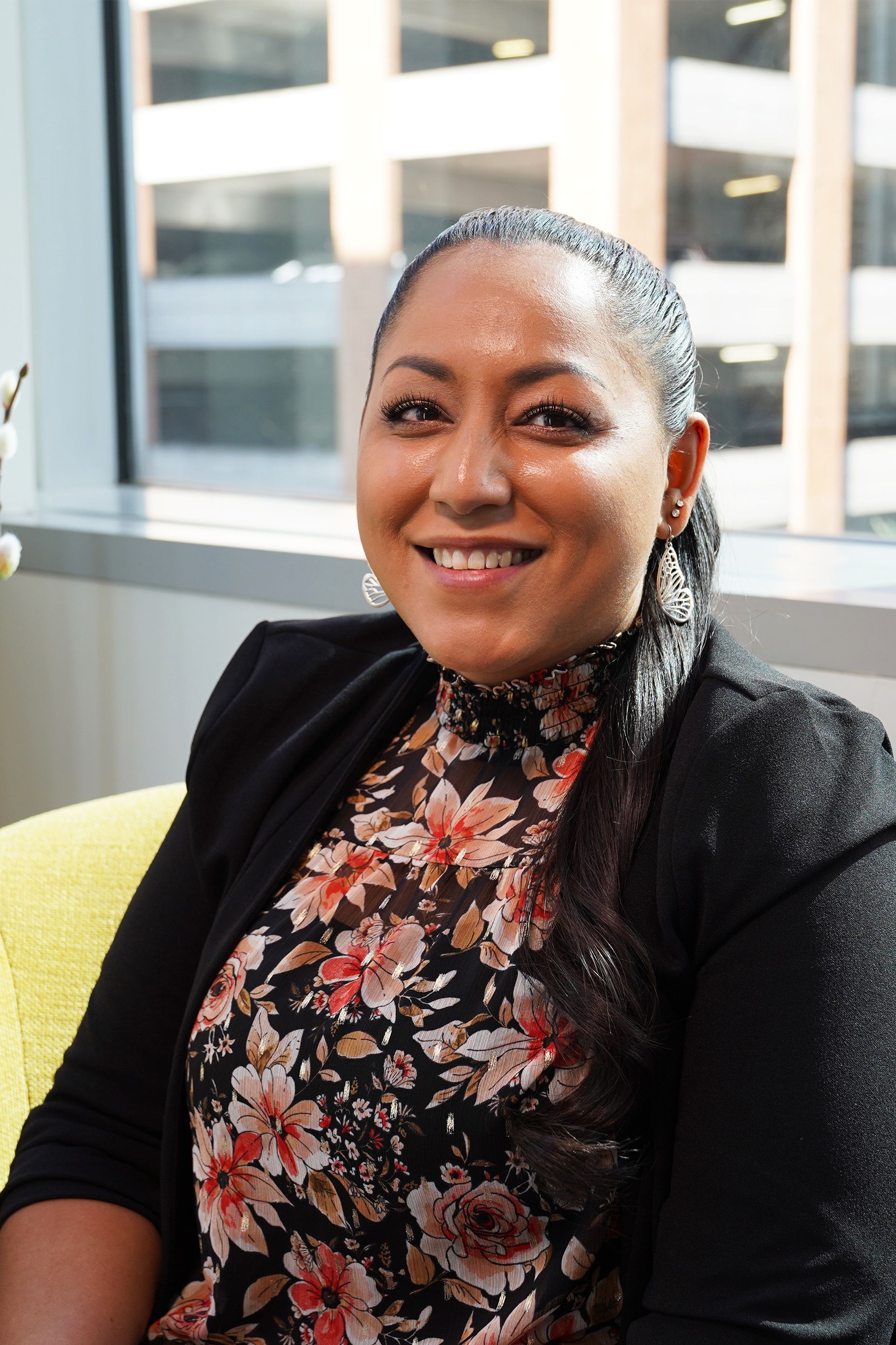 A woman is sitting in a chair in front of a window and smiling.