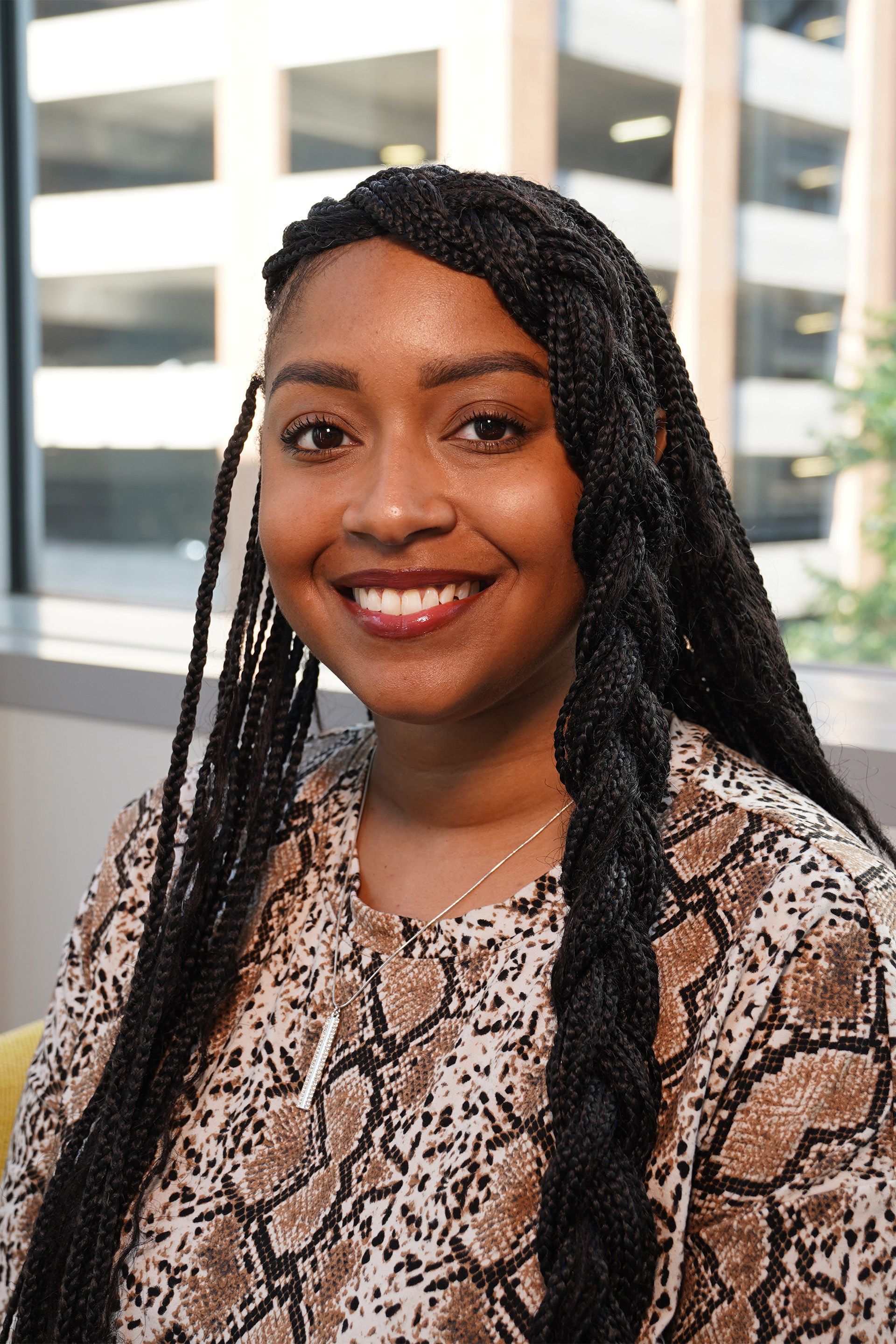 A woman with braids is smiling for the camera while wearing a snake print shirt.