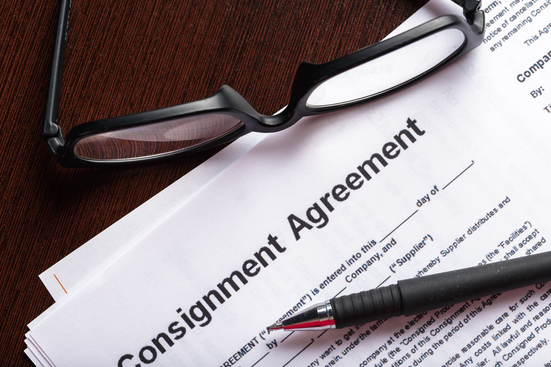 Consignment Agreement document, pen, and glasses on a brown surface.